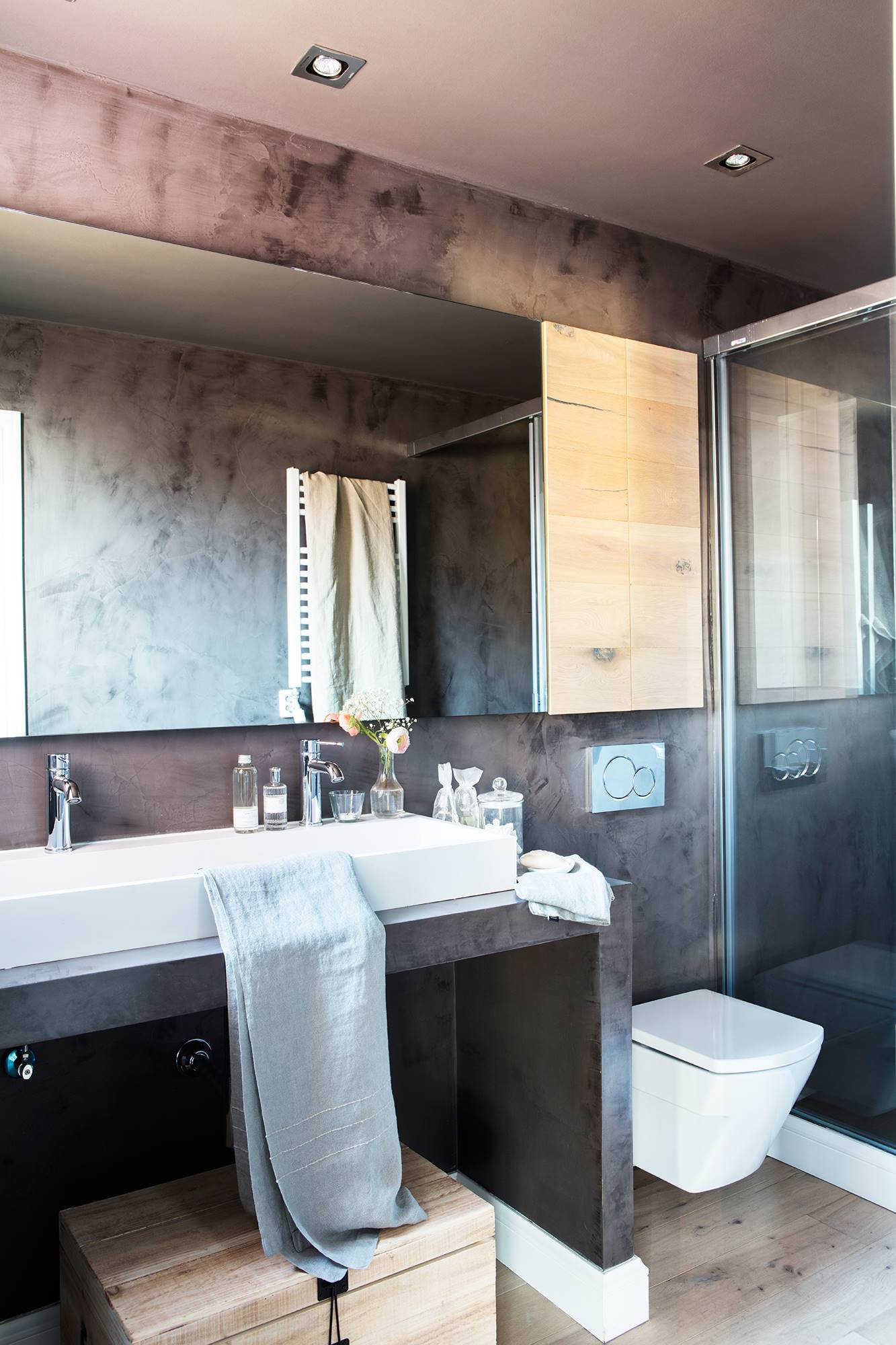 Baño con pared de microcemento gris y armarito de madera sobre el inodoro_ 00451981