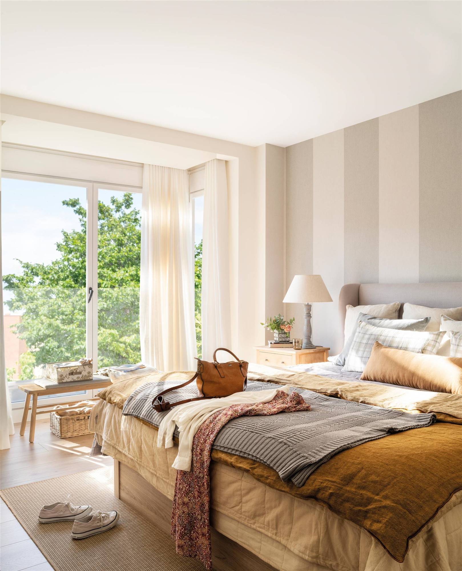 Dormitorio moderno con cabecero orejero en gris y pared revestida de papel pintado a rayas.