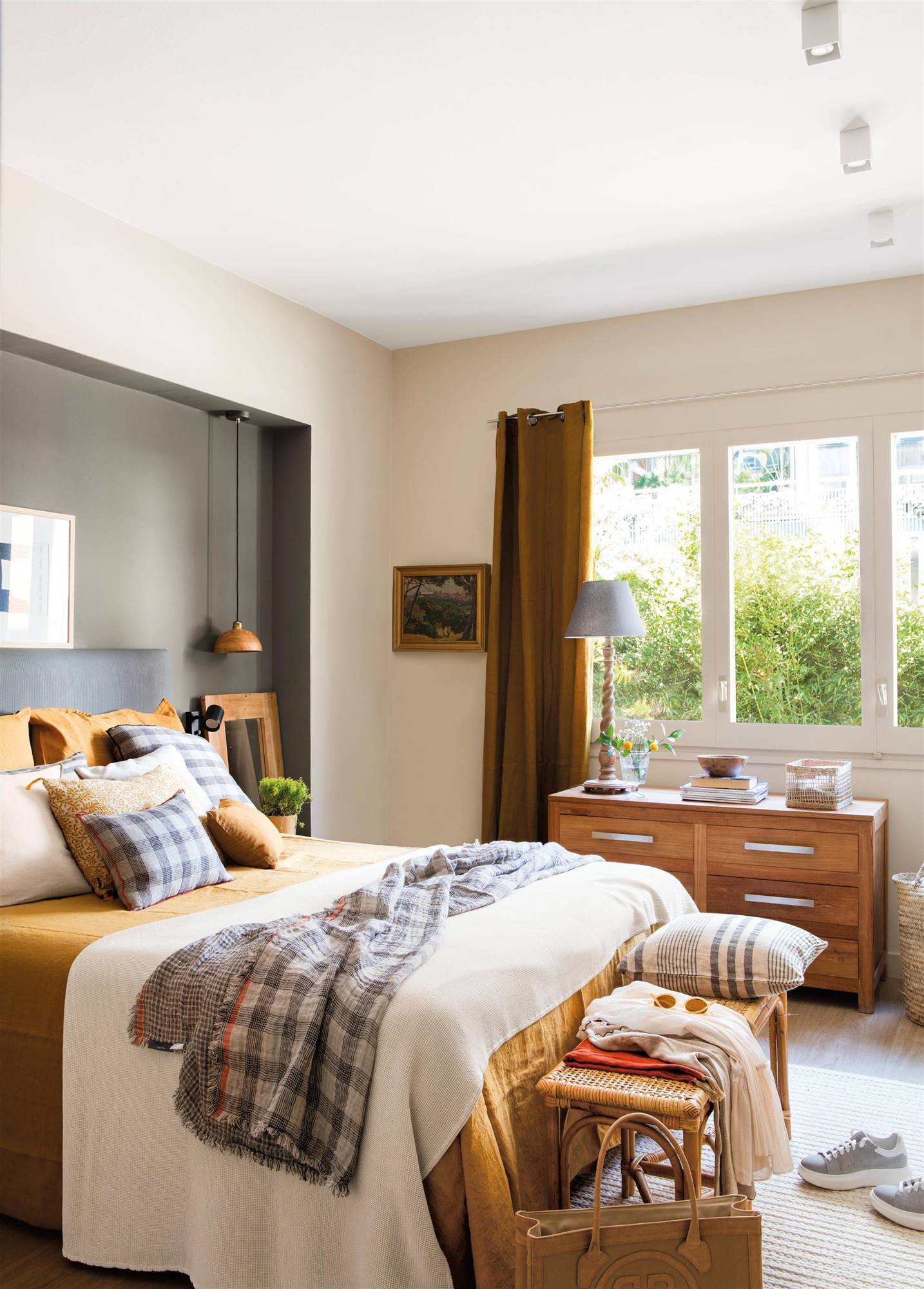 Dormitorio con cabecero tapizado y pared pintada de gris y cómoda bajo la ventana.