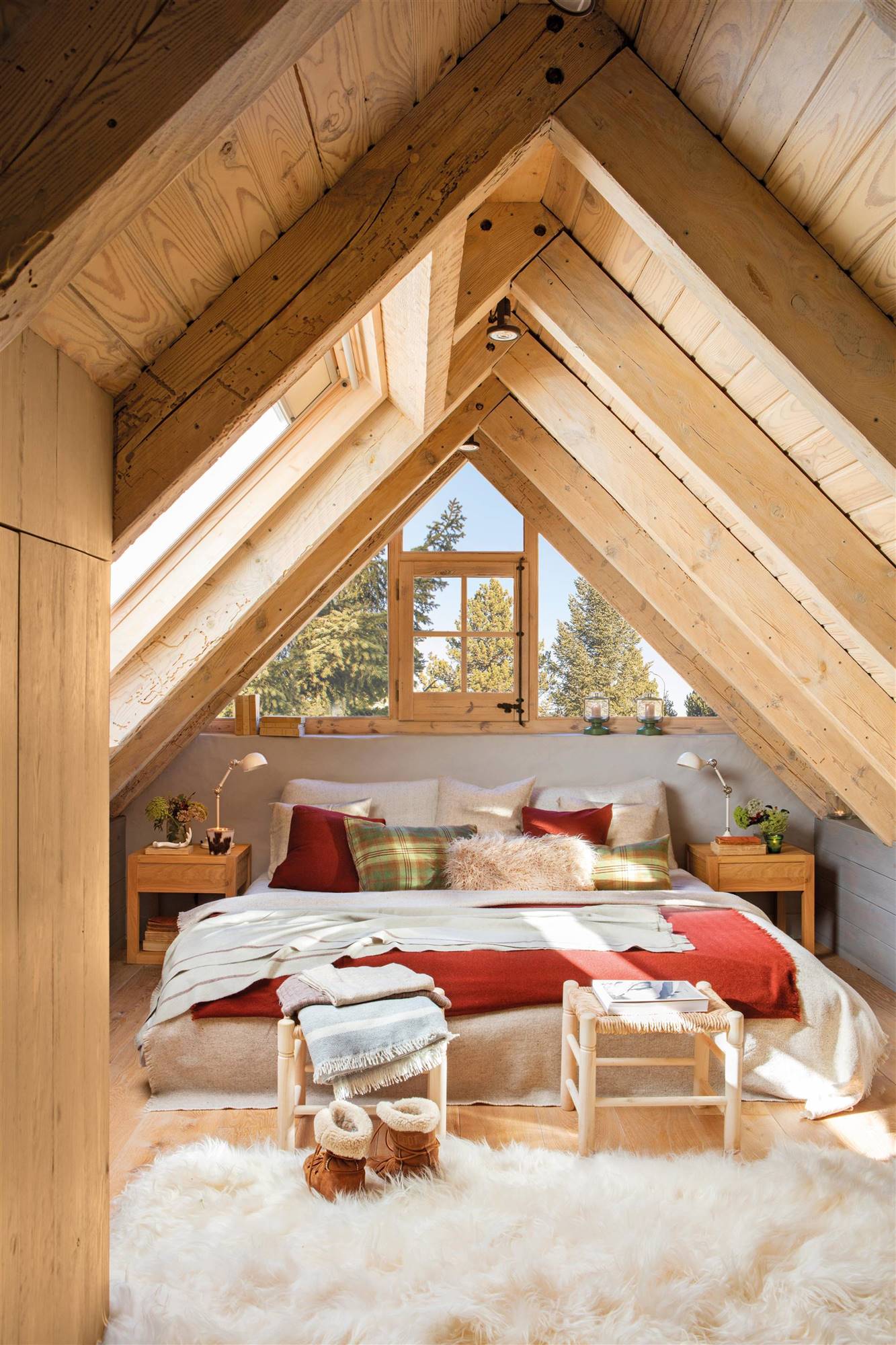 Dormitorio abuhardillado con vigas de madera y dos banqquetas a los pies de la cama.
