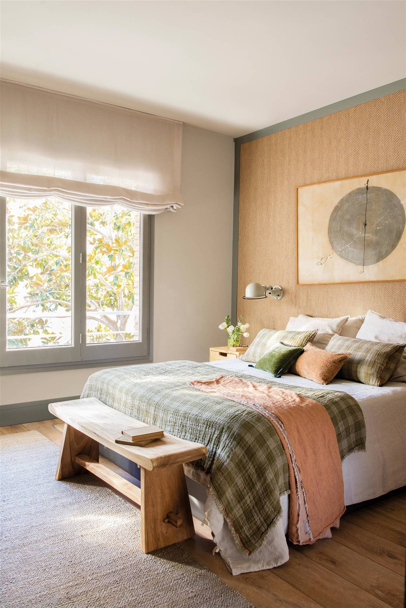 Dormitorio con pared de cabecero revestido de moqueta, cuadro, banco de madera y colcha de cuadros.