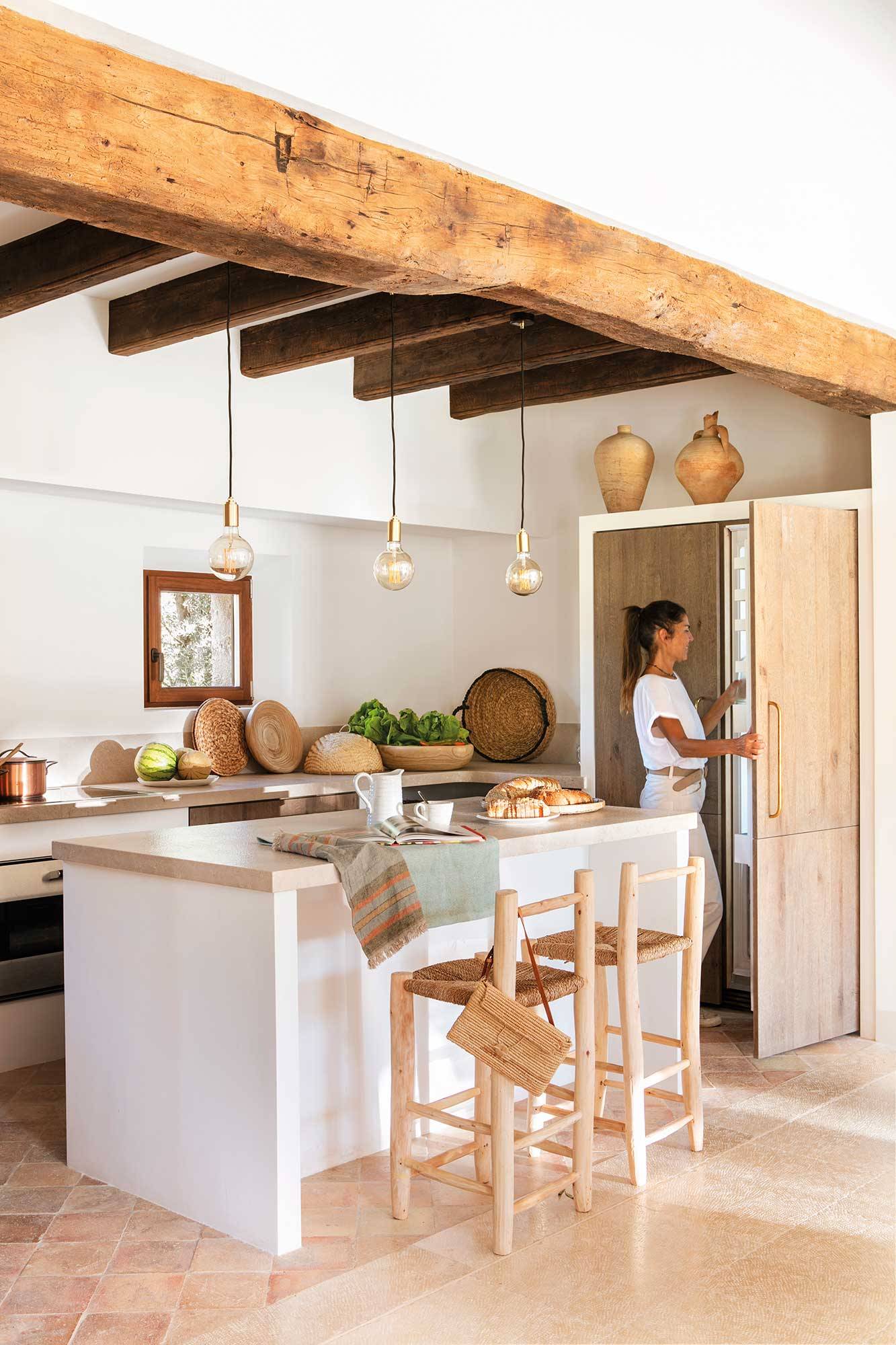 Cocina rústica abierta de color blanco y techo con vigas de madera. 