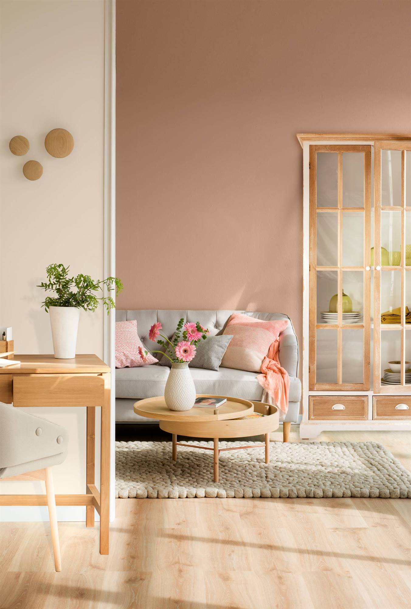 Salón con pared rosa y sofá gris con mesa de centro, consola y armario en madera clara.