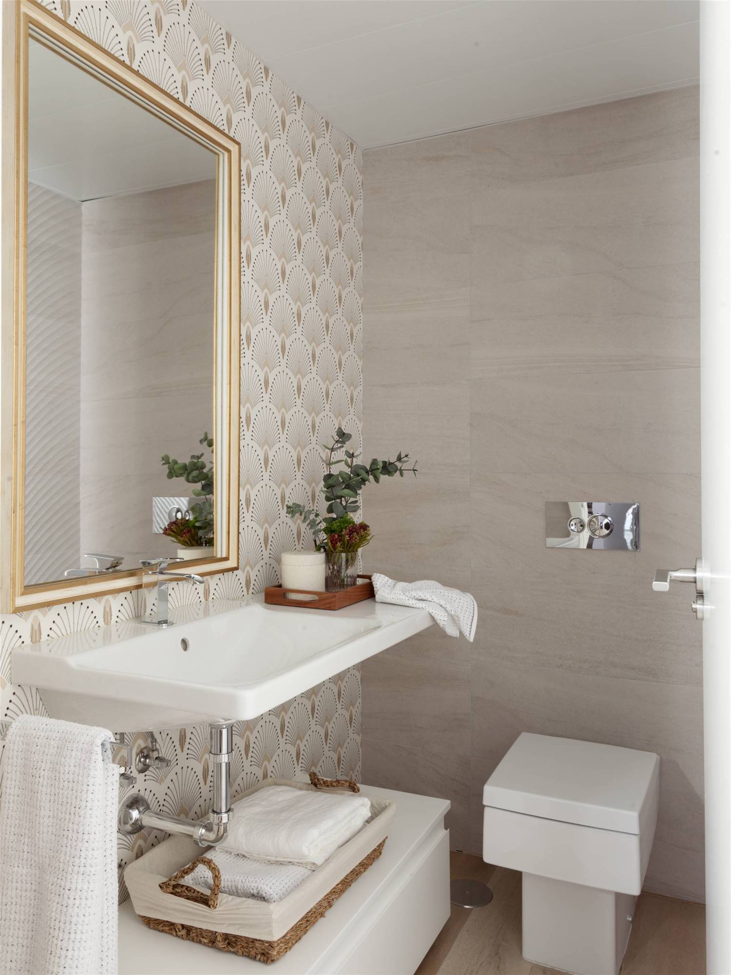 Baño con papel pintado en la pared del lavabo y inodoro con cisterna empotrada. 