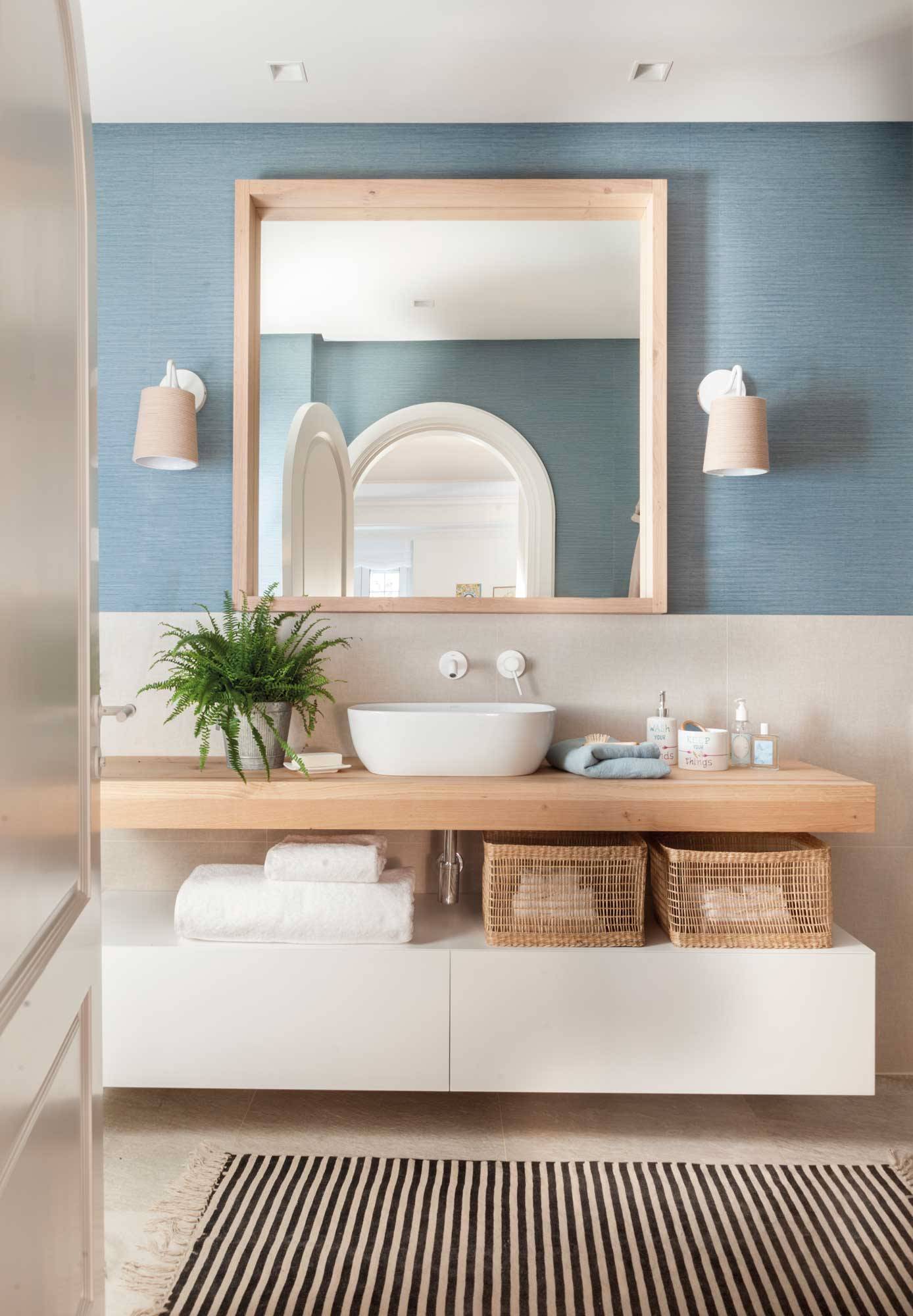 Baño con papel pintado azul, encimera de madera y mueble de baño blanco. 