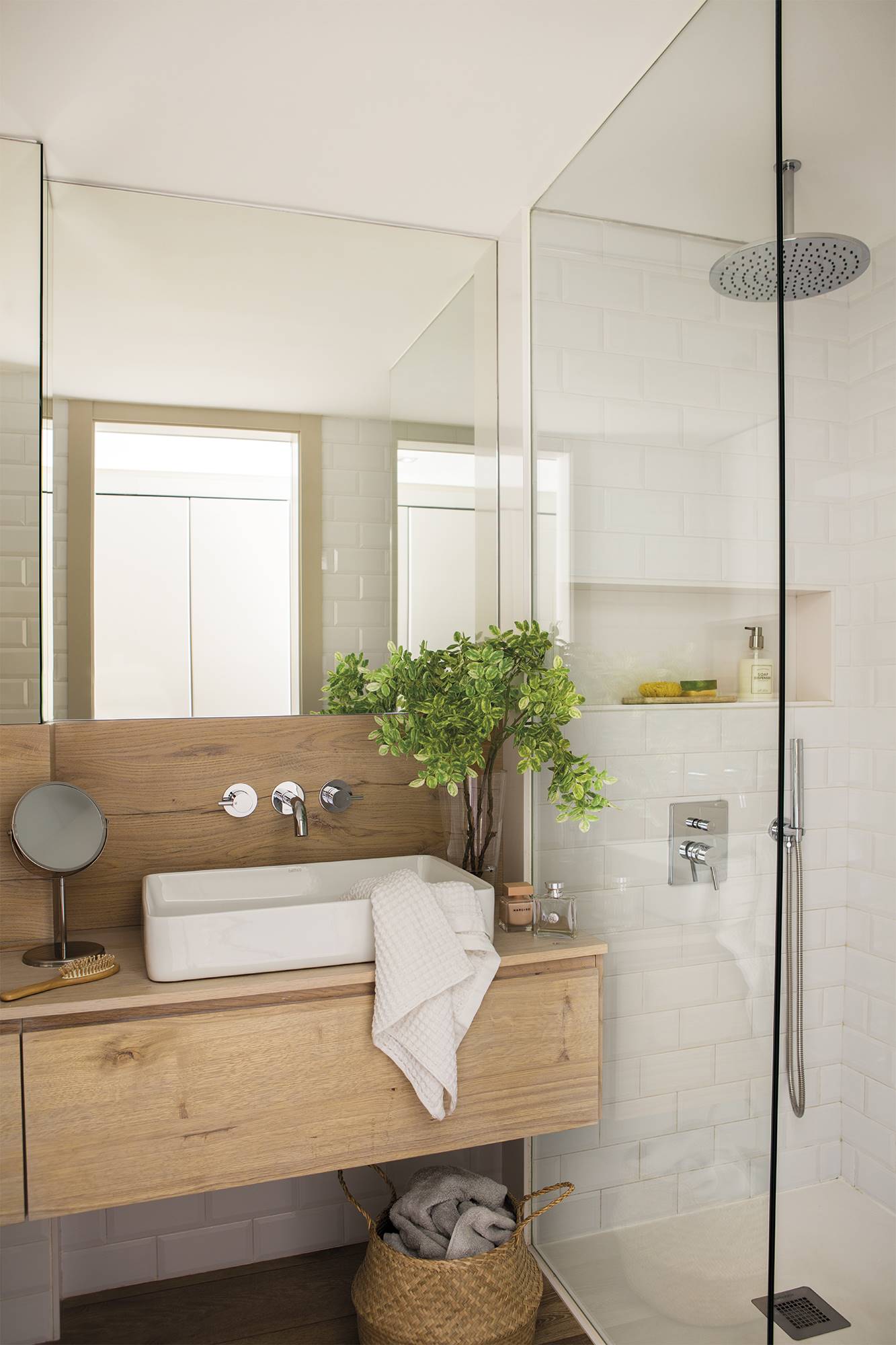 Baño con mueble de madera y ducha con revestimiento blanco y panel fijo. 