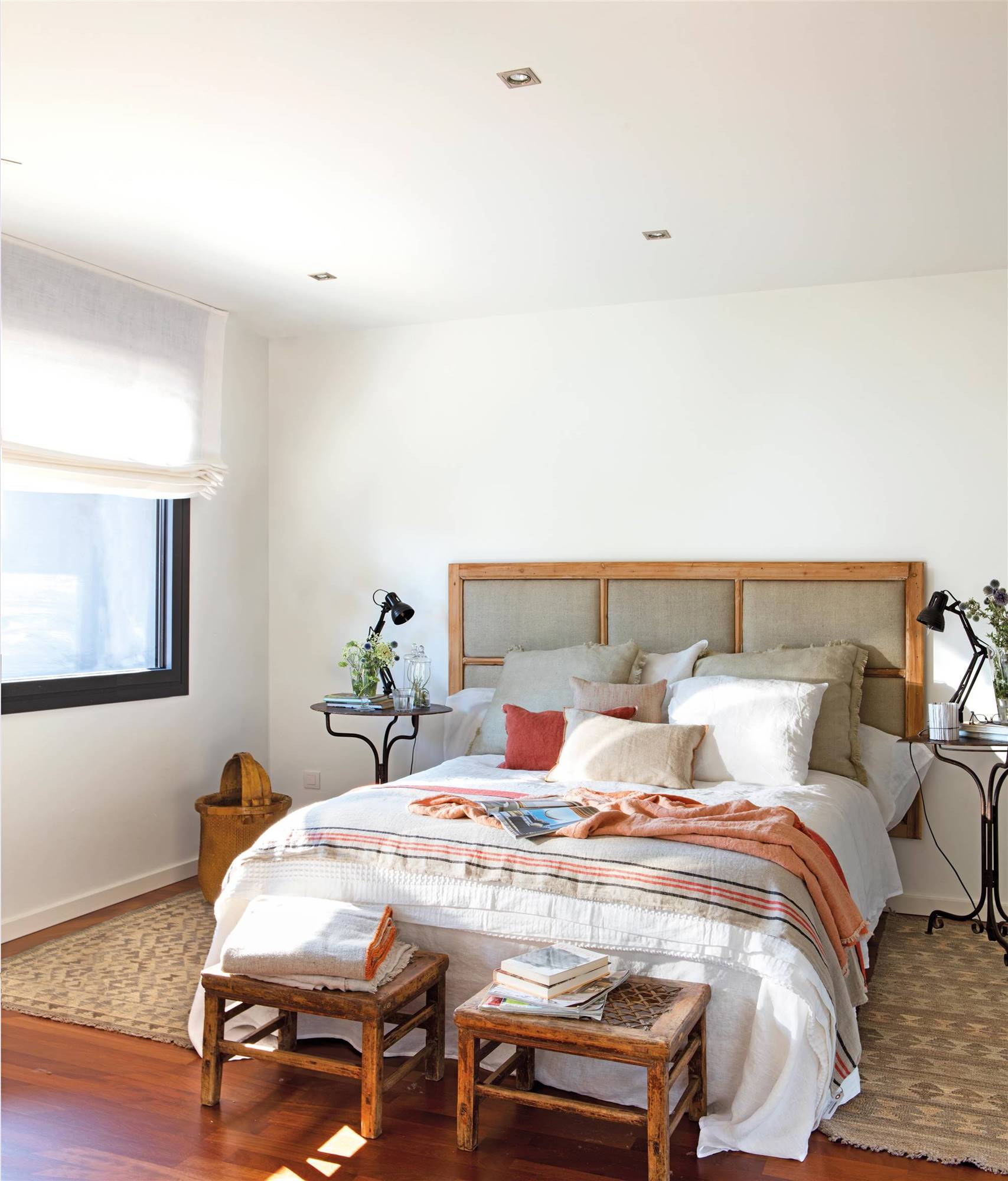Dormitorio con banquetas, alfombras y cabecero realizado con una antigua puerta de cuarterones.