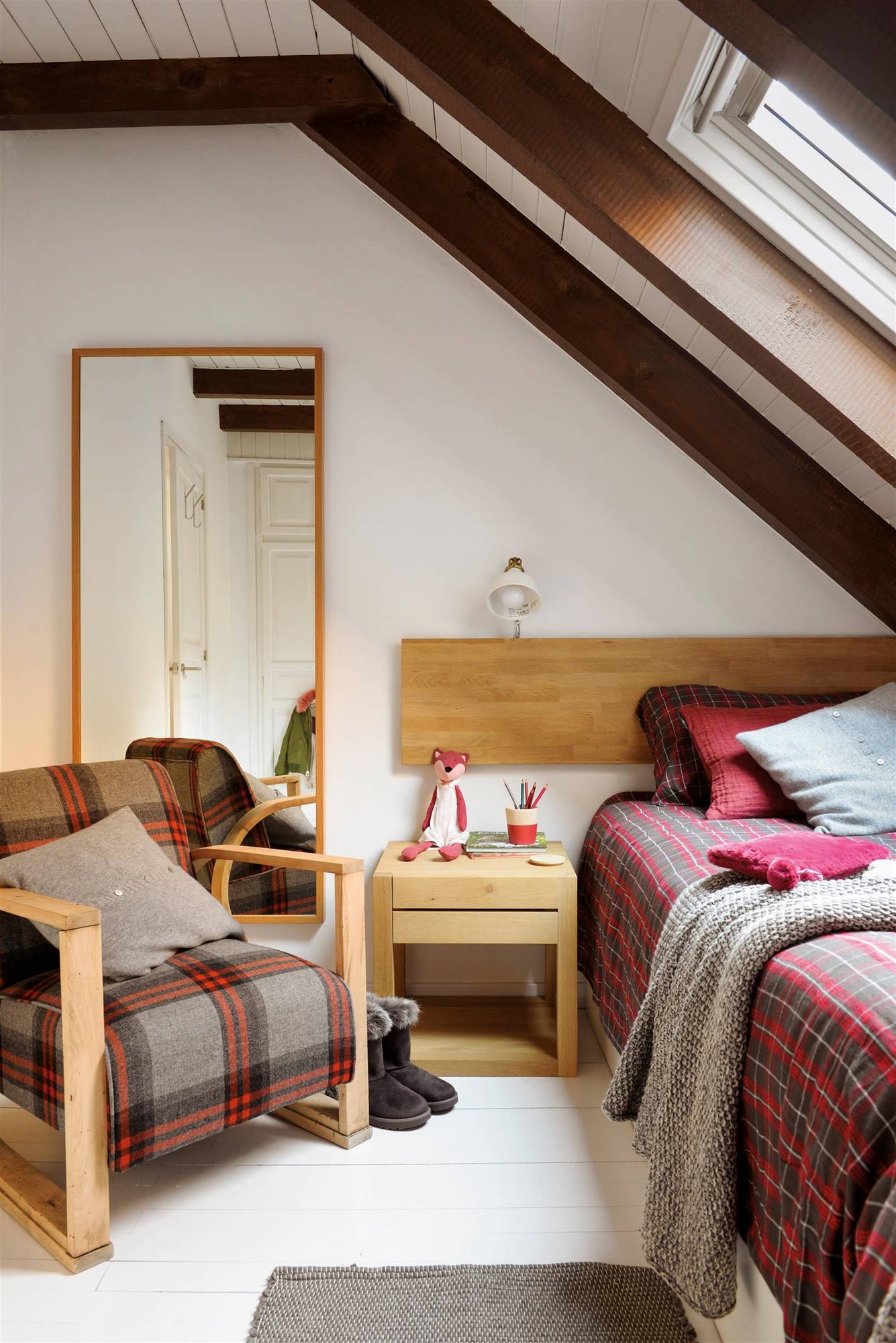 Dormitorio rústico con butaca, ropa de cama de cuadros y cabecero hecho con tablero de madera.