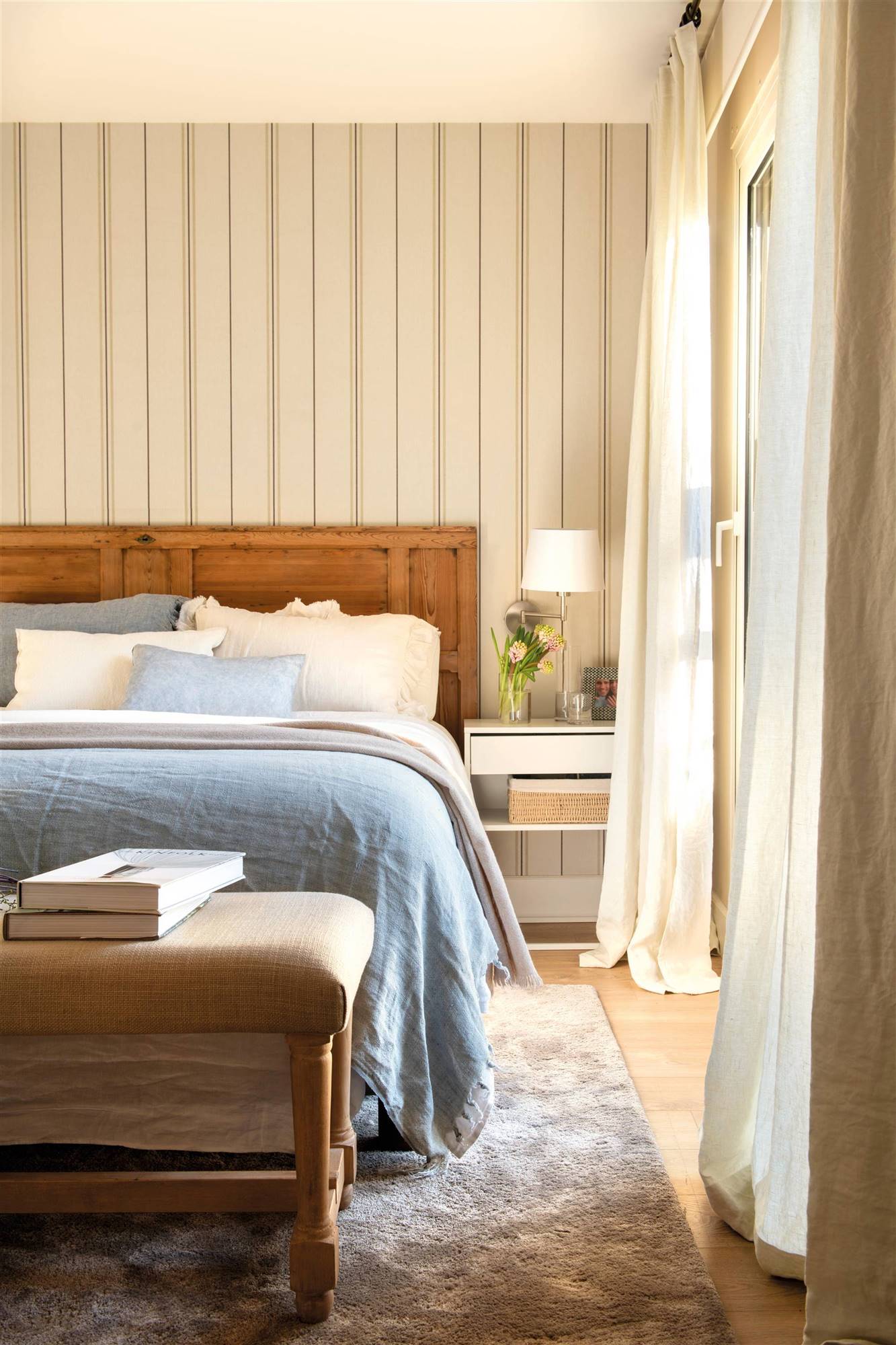 Dormitorio con papel pintado, banqueta y cabecero de madera. 