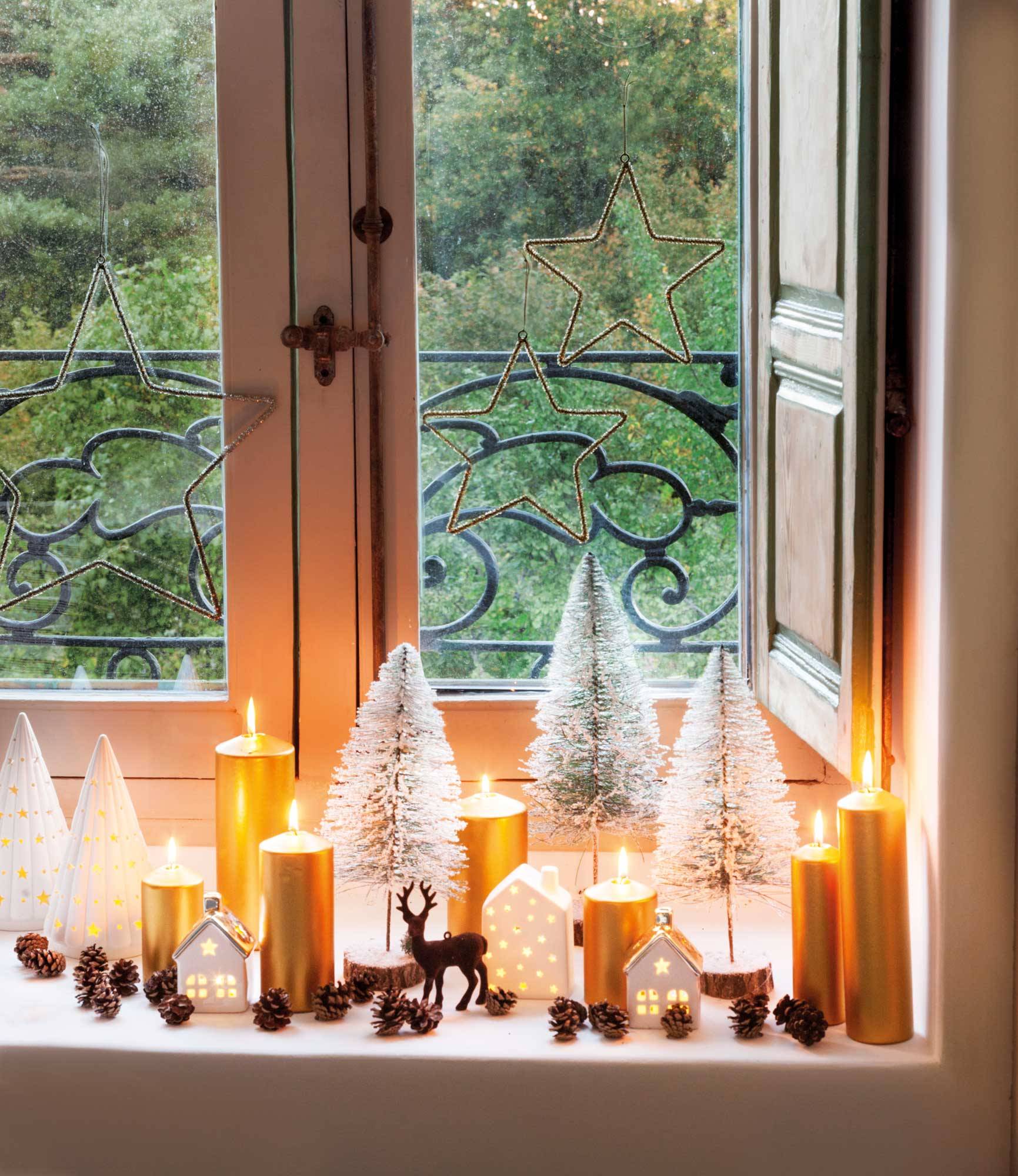 Ventana con adornos navideños de velas, arbolitos y piñas.