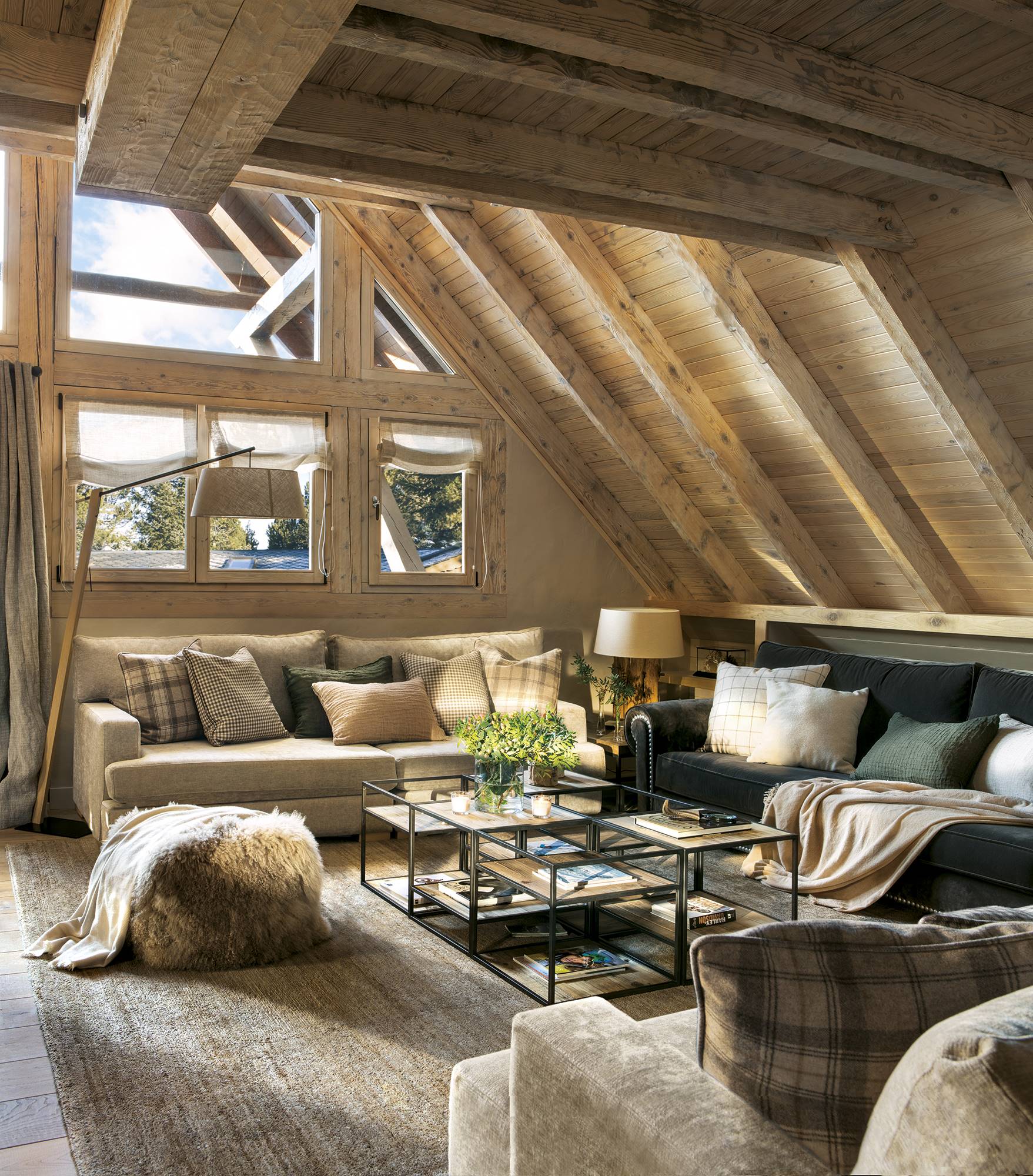 Salón rústico abuhardillado con revestimiento de madera y un sofá verde y otro beige. 