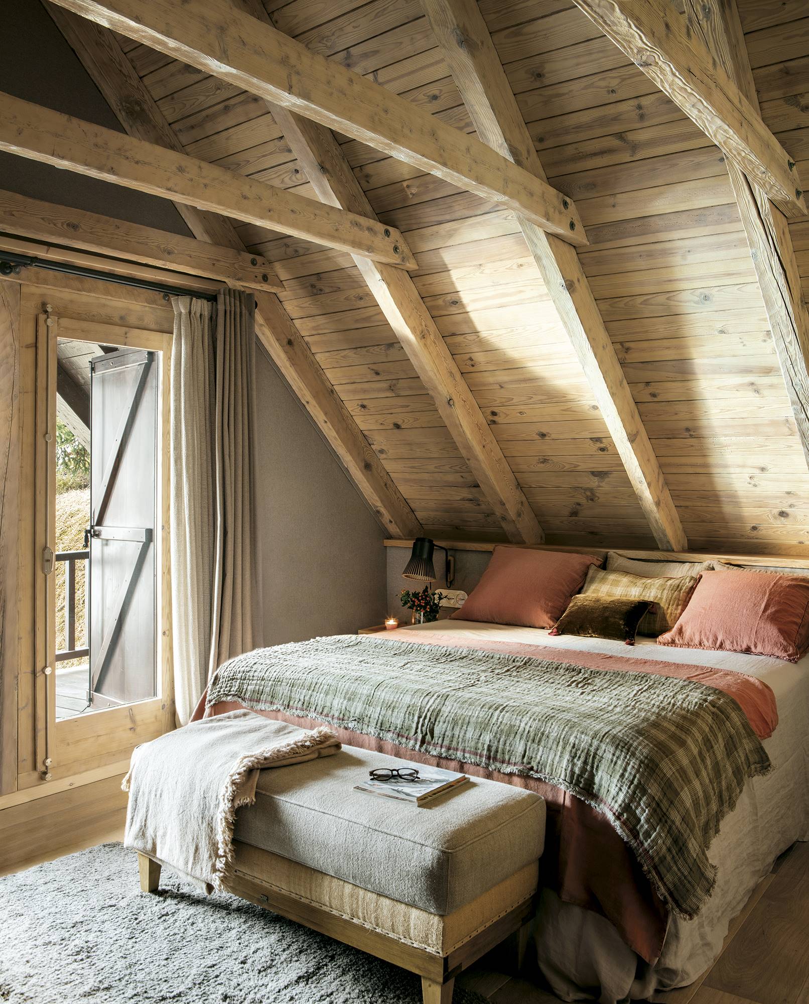 Dormitorio rústico abuhardillado con paredes y techos de madera y banco a los pies de la cama.  