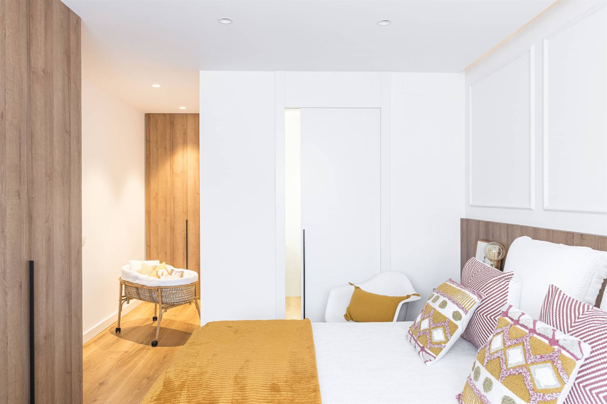 Dormitorio principal después de la reforma con armario y suelos de madera, ropa de cama con detalles mostaza y baño privado. 