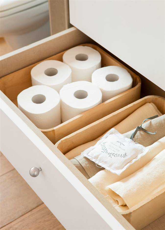 Detalle de cajón de mueble bajolavabo con papel higiénico y toallas dobladas y guardadas en vertical. 