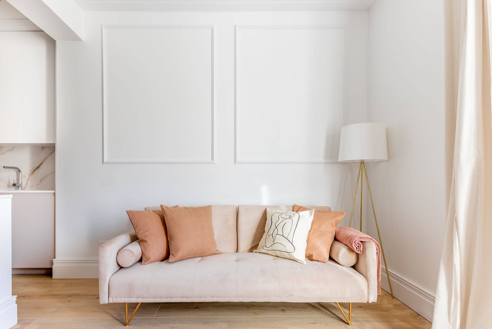 Salón blanco con molduras y sofá rosa empolvado de diseño moderno con cojines y lámpara de pie dorada. 