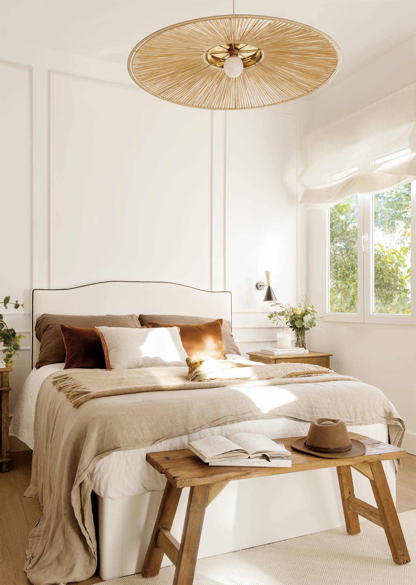 Dormitorio principal con pared con molduras, banco de madera al pie de la cama y lámpara original. 
