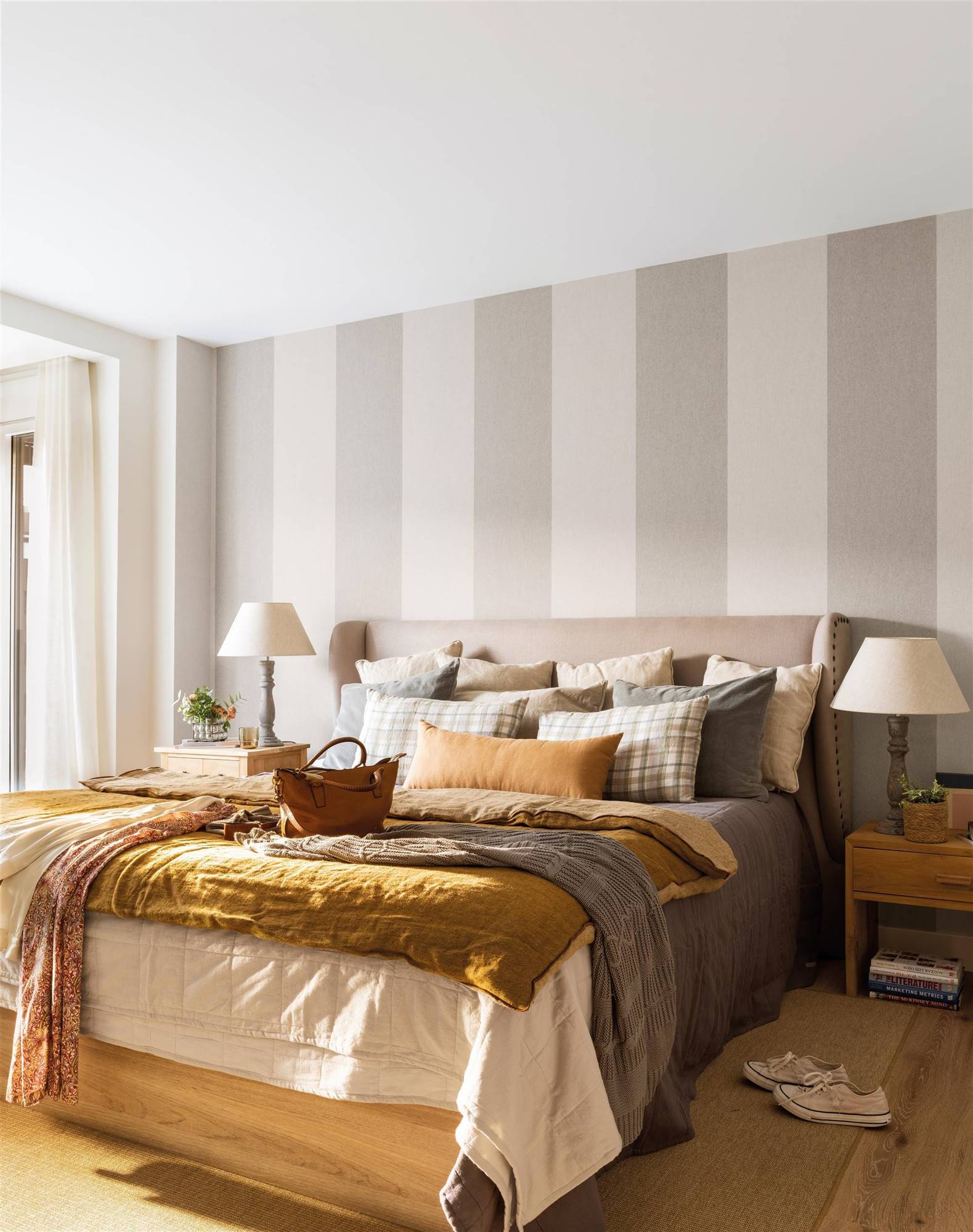 Dormitorio clásico con papel pintado de rayas y cabecero tapizado. 