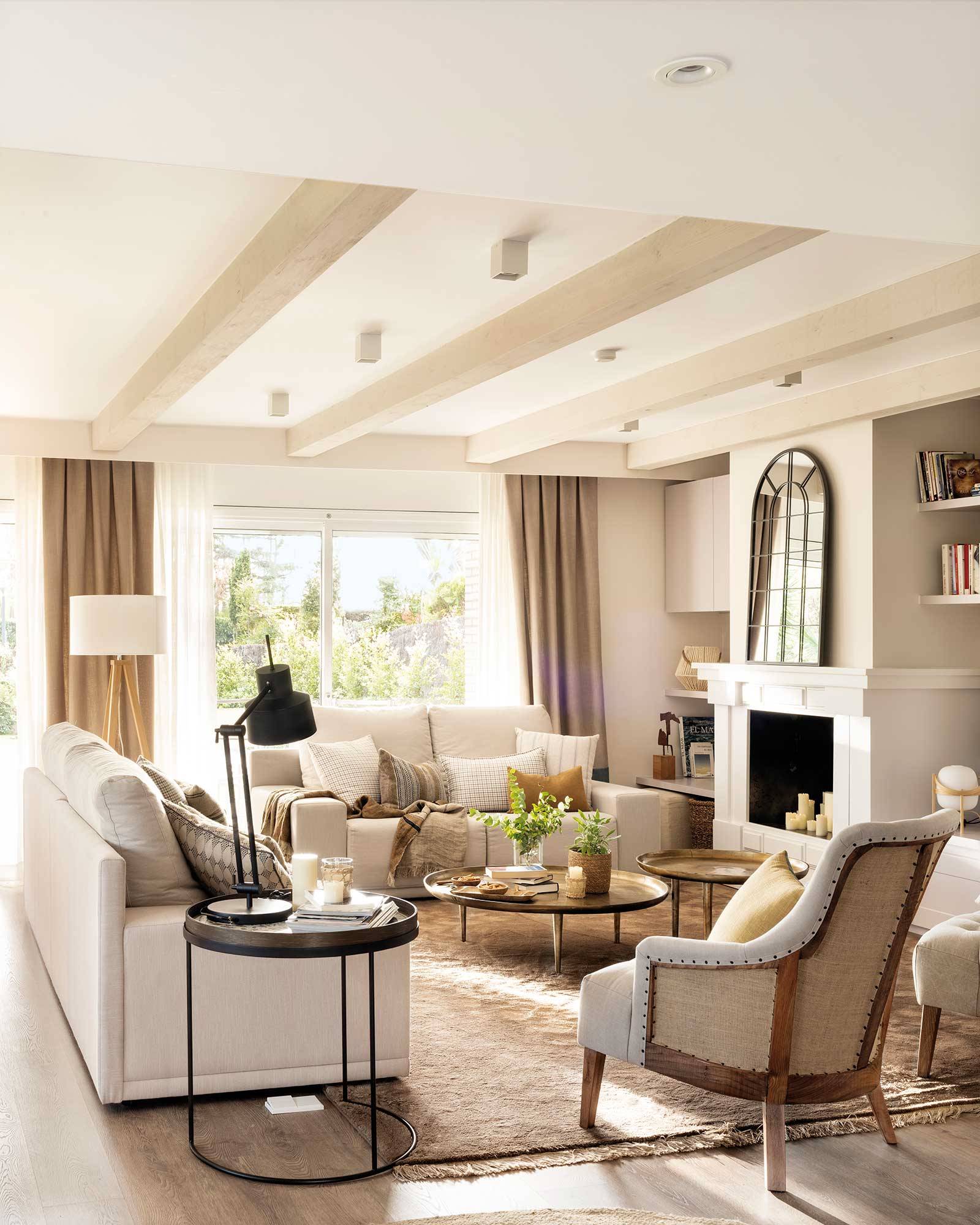 Salón con sofás blancos, butaca gris, alfombra, chimenea, espejo cuarterones y vigas en el techo. 