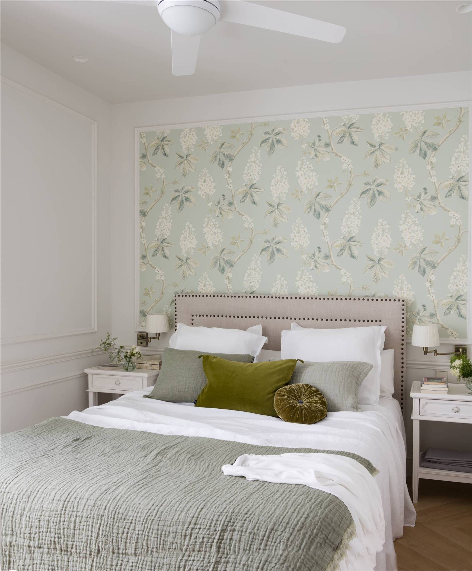 Dormitorio con cabecero tapizado con tachuelas y papel pintado con estampado floral en la pared. 