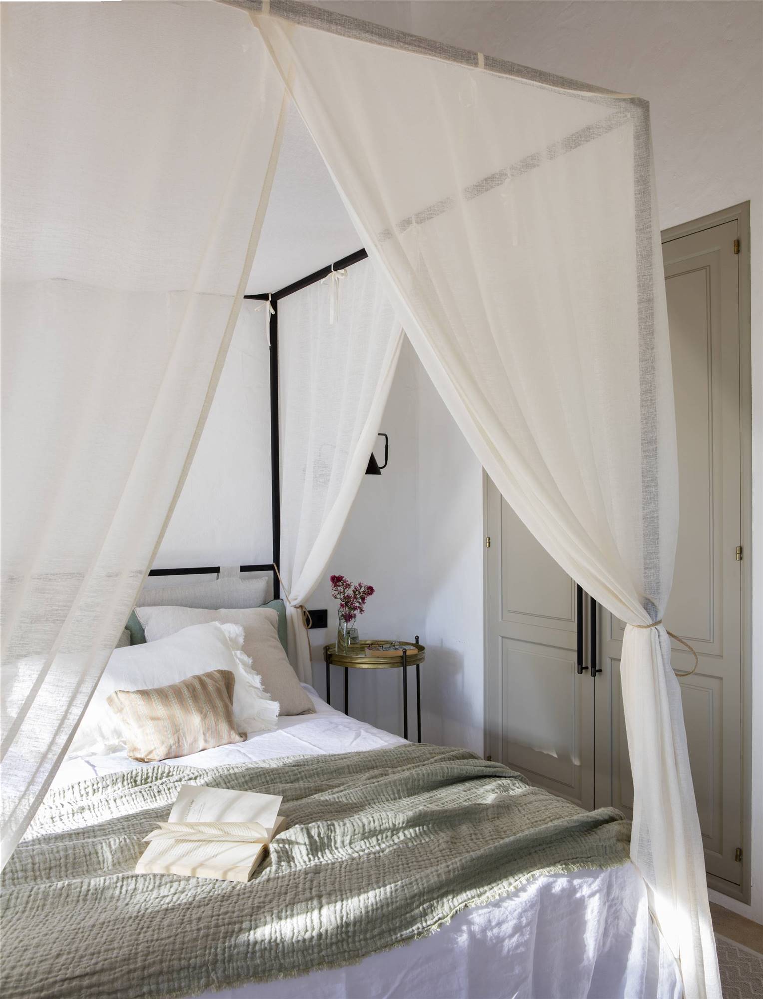 Dormitorio con cama con dosel de hierro y cortinas blancas. 