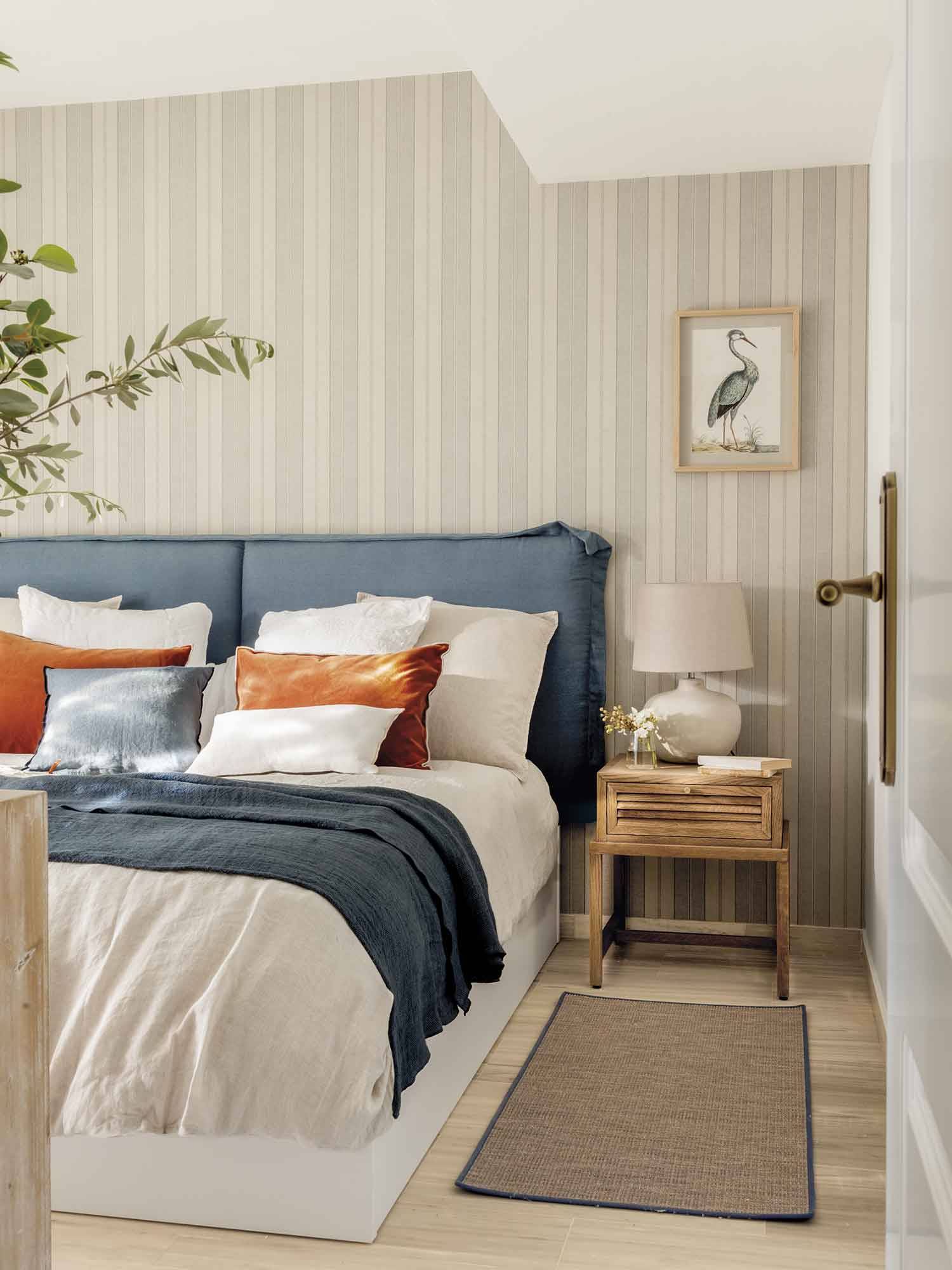 Dormitorio clásico con cabecero de lino de color azul y papel pintado de rayas.  