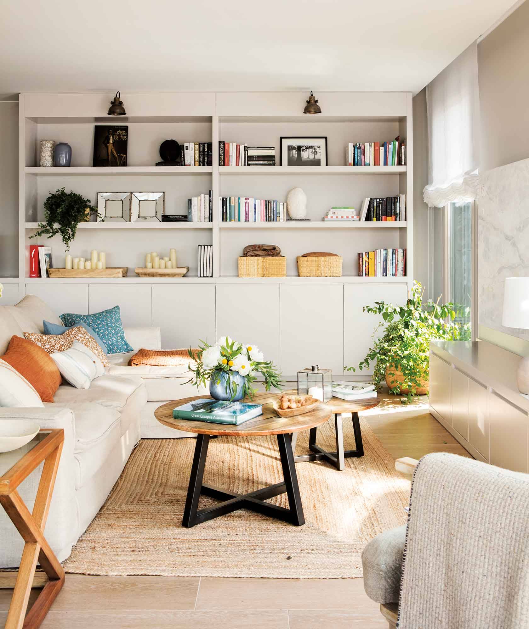 Salón con librerías en gris, alfombra de fibras, sofá claro con chaise longue y mesa de centro de madera.