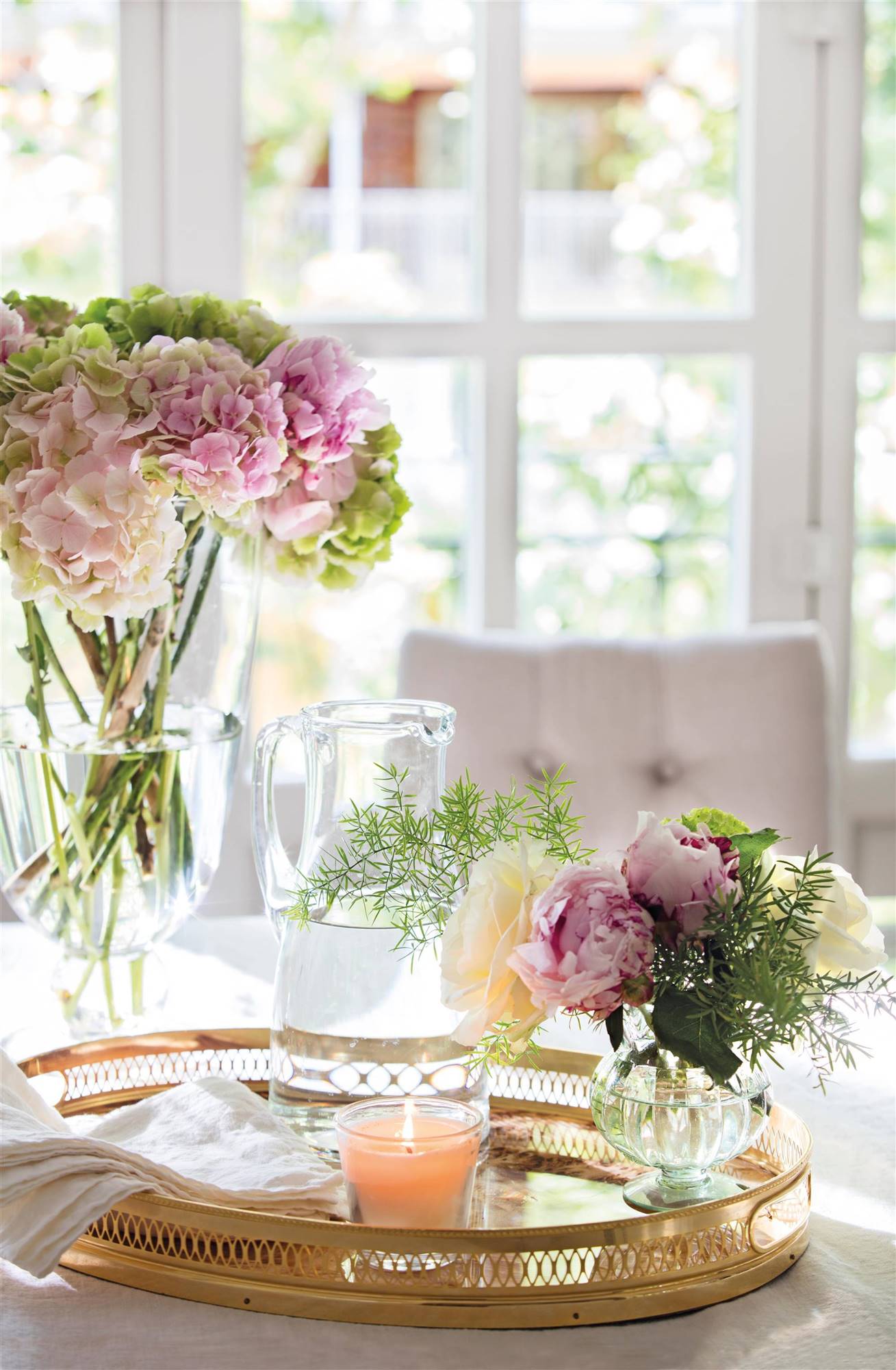 Detalle de mesa con jarrón con flores, bandeja dorada y vela.