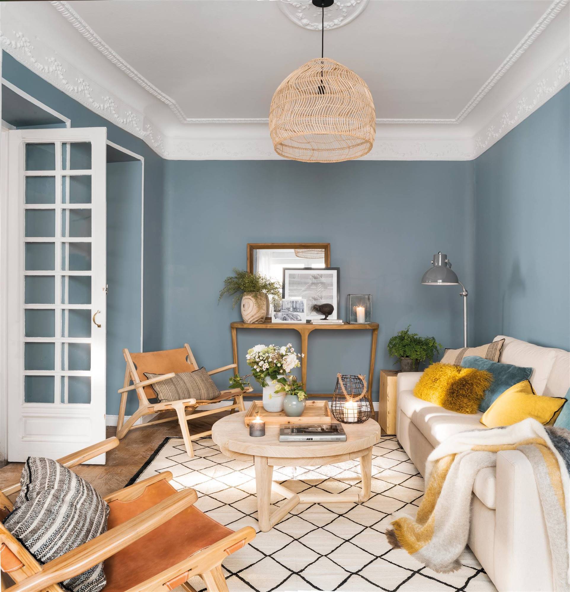 Salón con paredes azules, sofá blanco, mesa de centro redondas de madera, butacas de piel y alfombra con motivos geométricos.