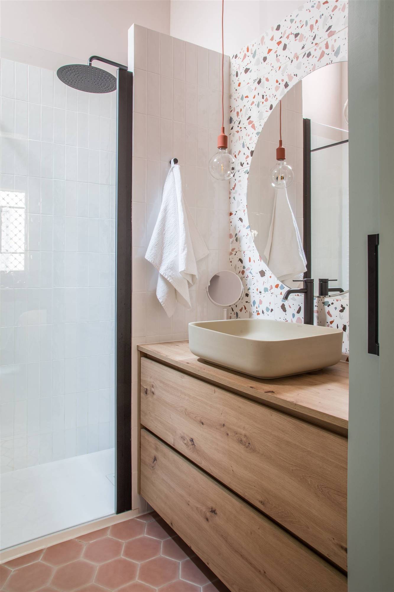 Baño con ducha, mueble de madera, espejo redondo y pared de terrazo