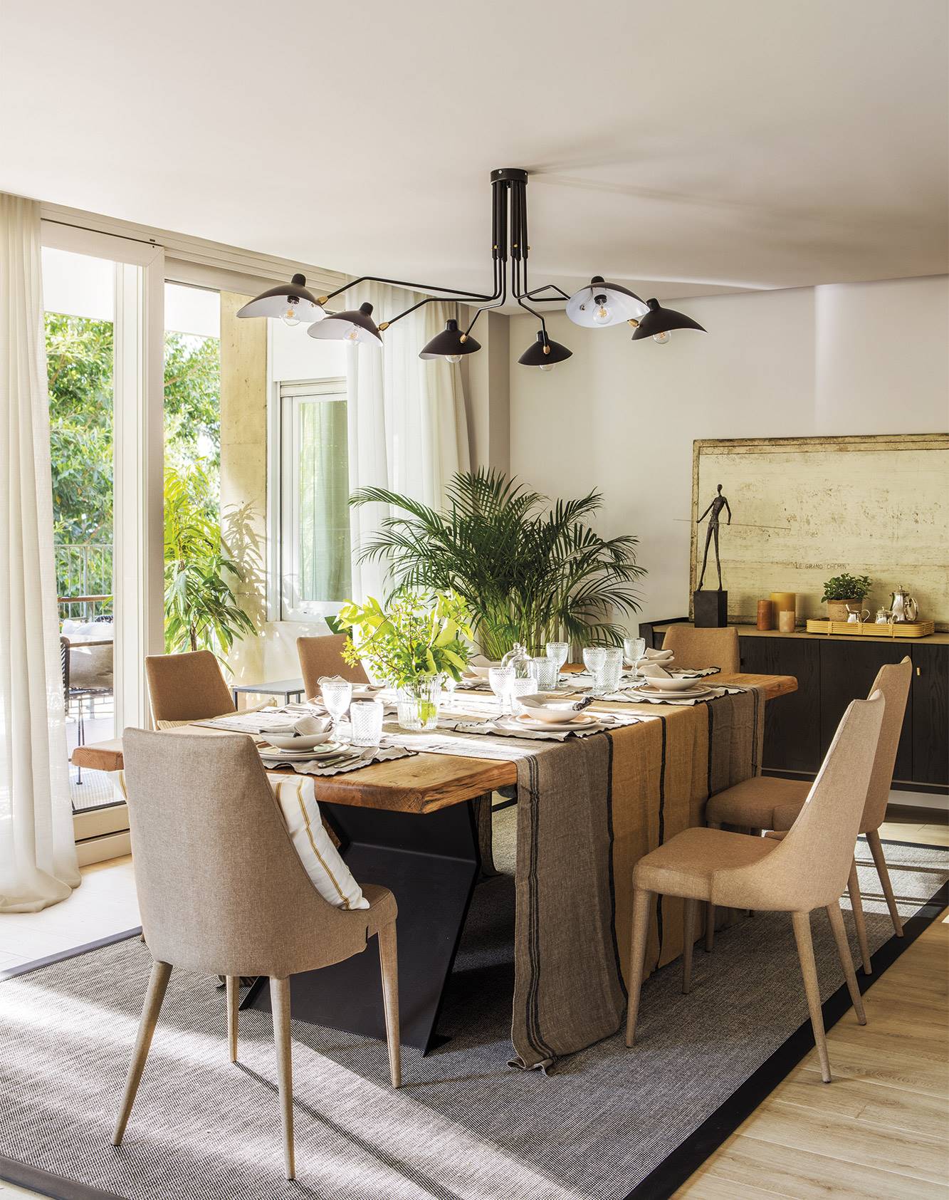 Comedor con mesa de madera, sillas tapizadas y lámpara negra de estilo moderno.  