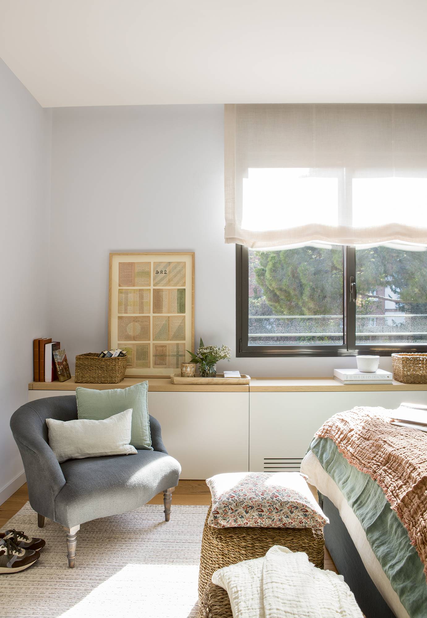 Dormitorio con mueble blanco y de madera a medida bajo la ventana y una butaca para la lectura.