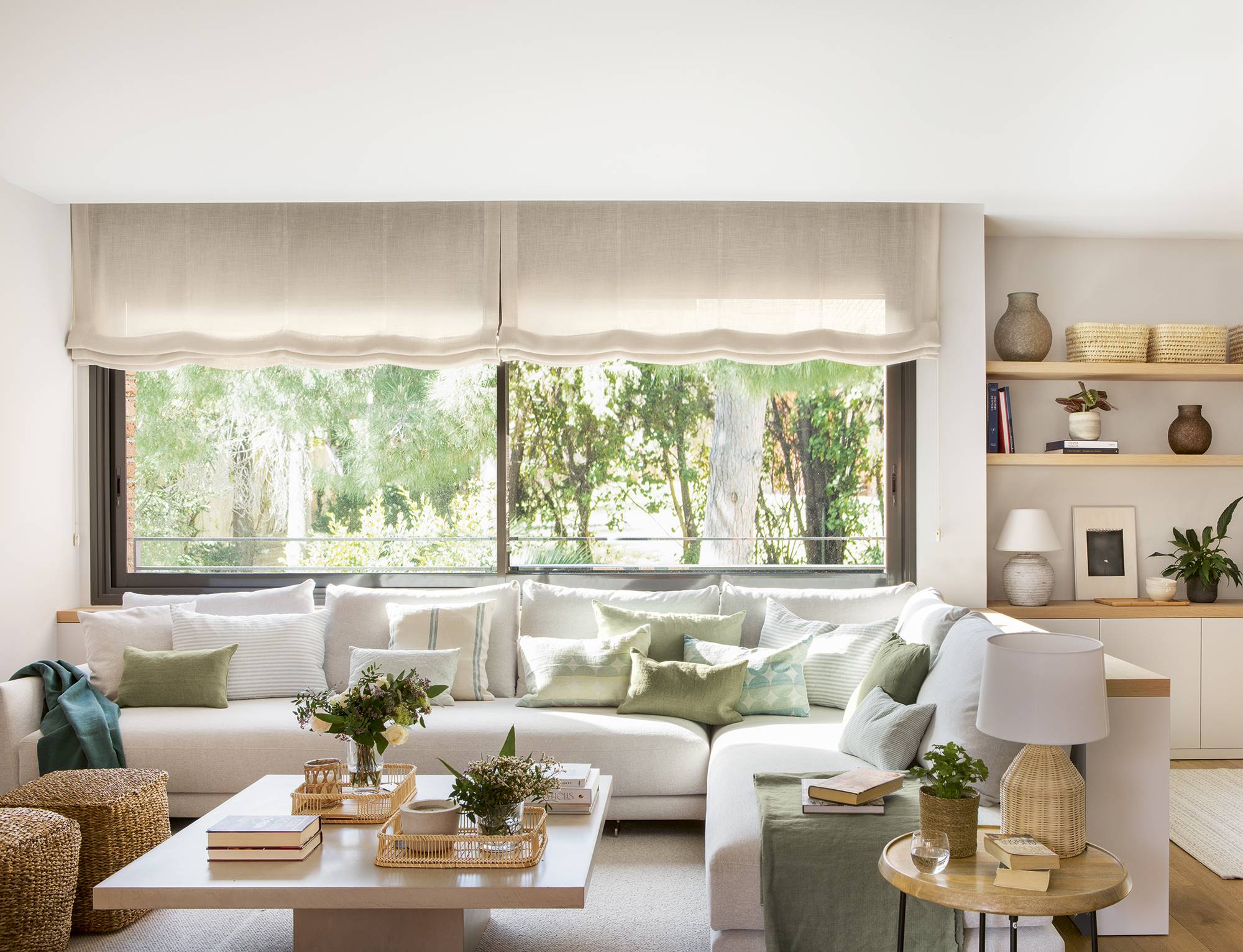 Salón blanco con sofá esquinero, pufs de fibras, cojines verdes y muebles a medida.