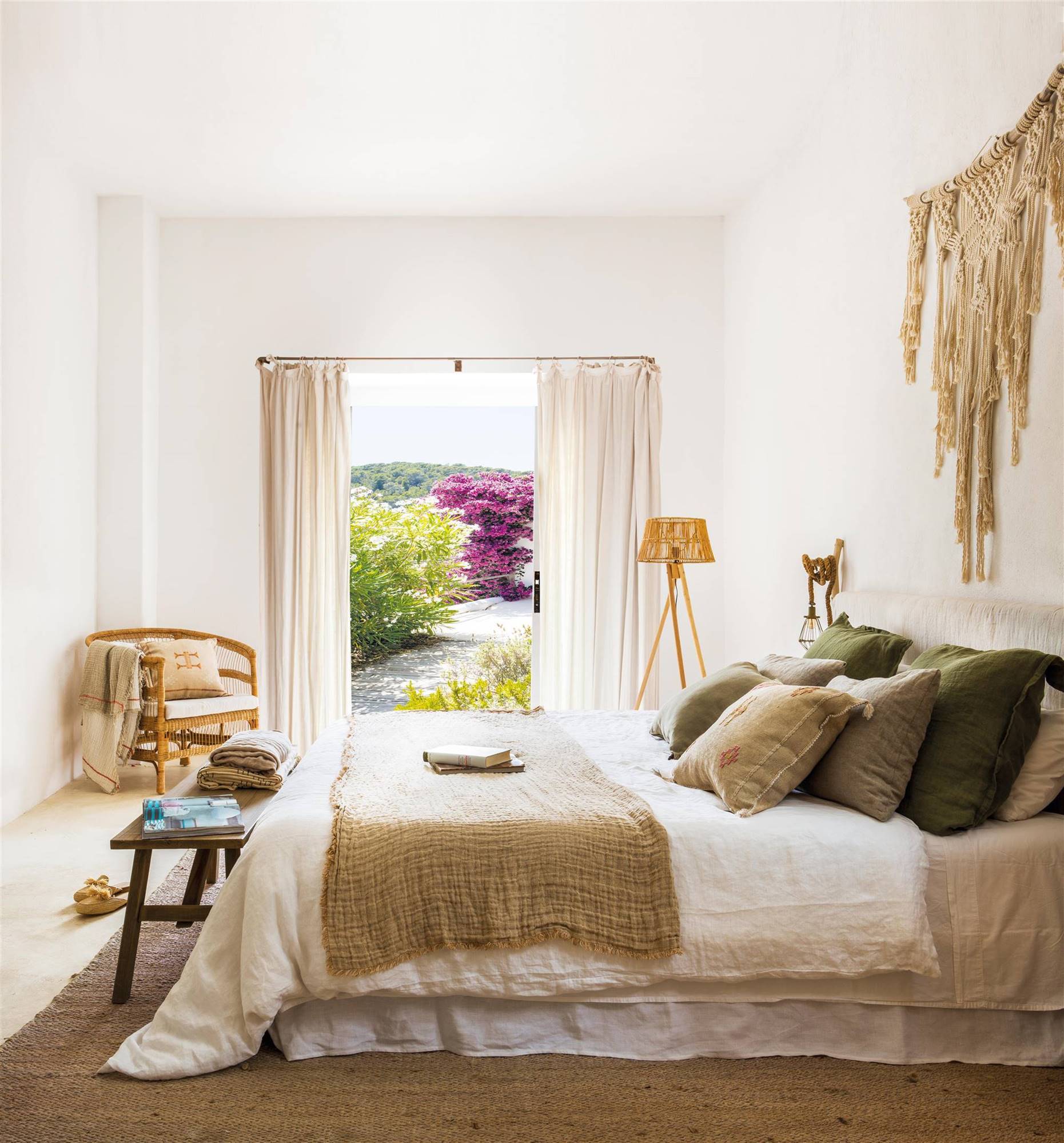 Dormitorio de verano con ropa de cama blanca y cojines y plaids en tonos tierra y verdes. 