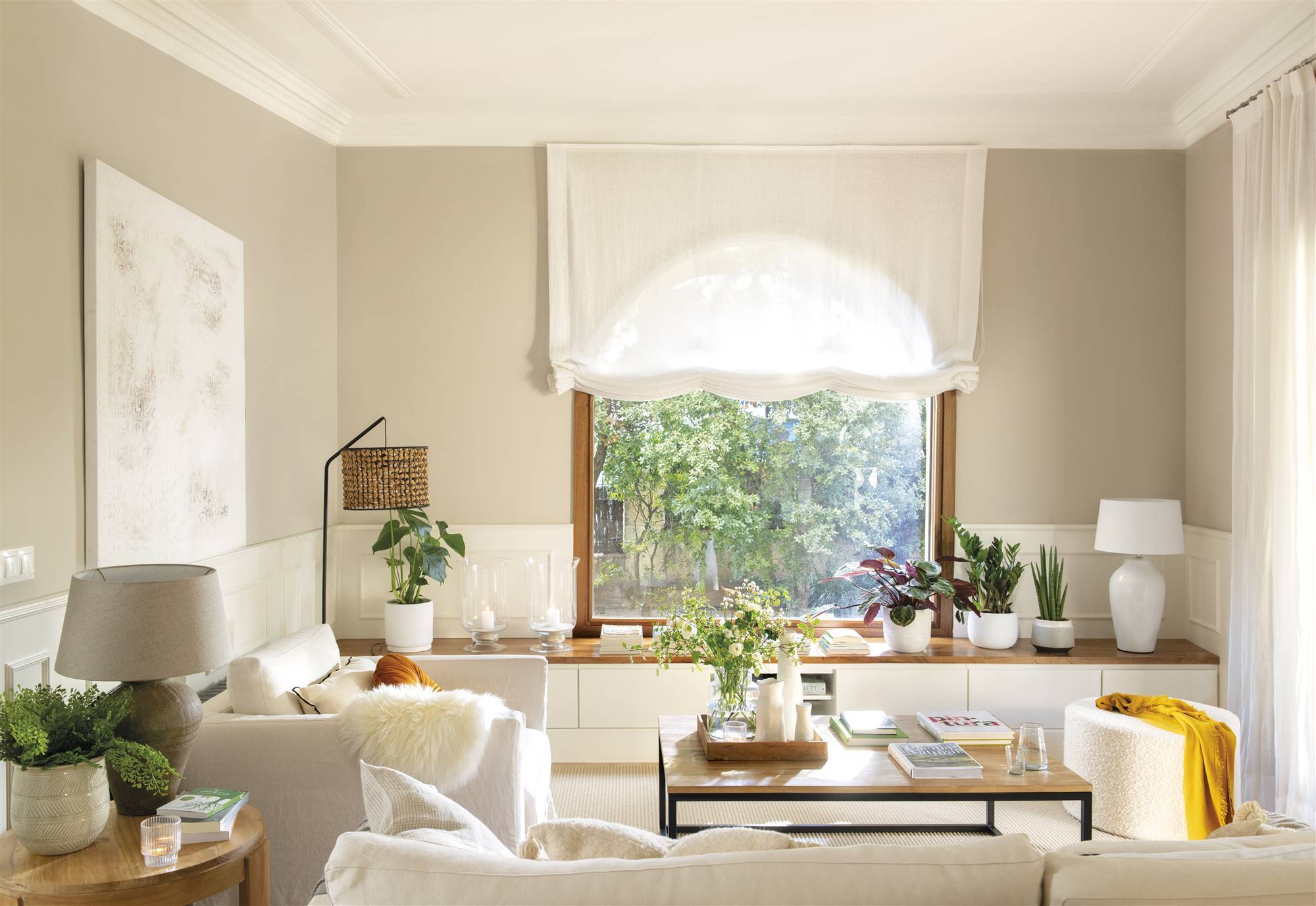 Salón pequeño con gran ventanal, paredes de color beige y pocos muebles de color blanco. 