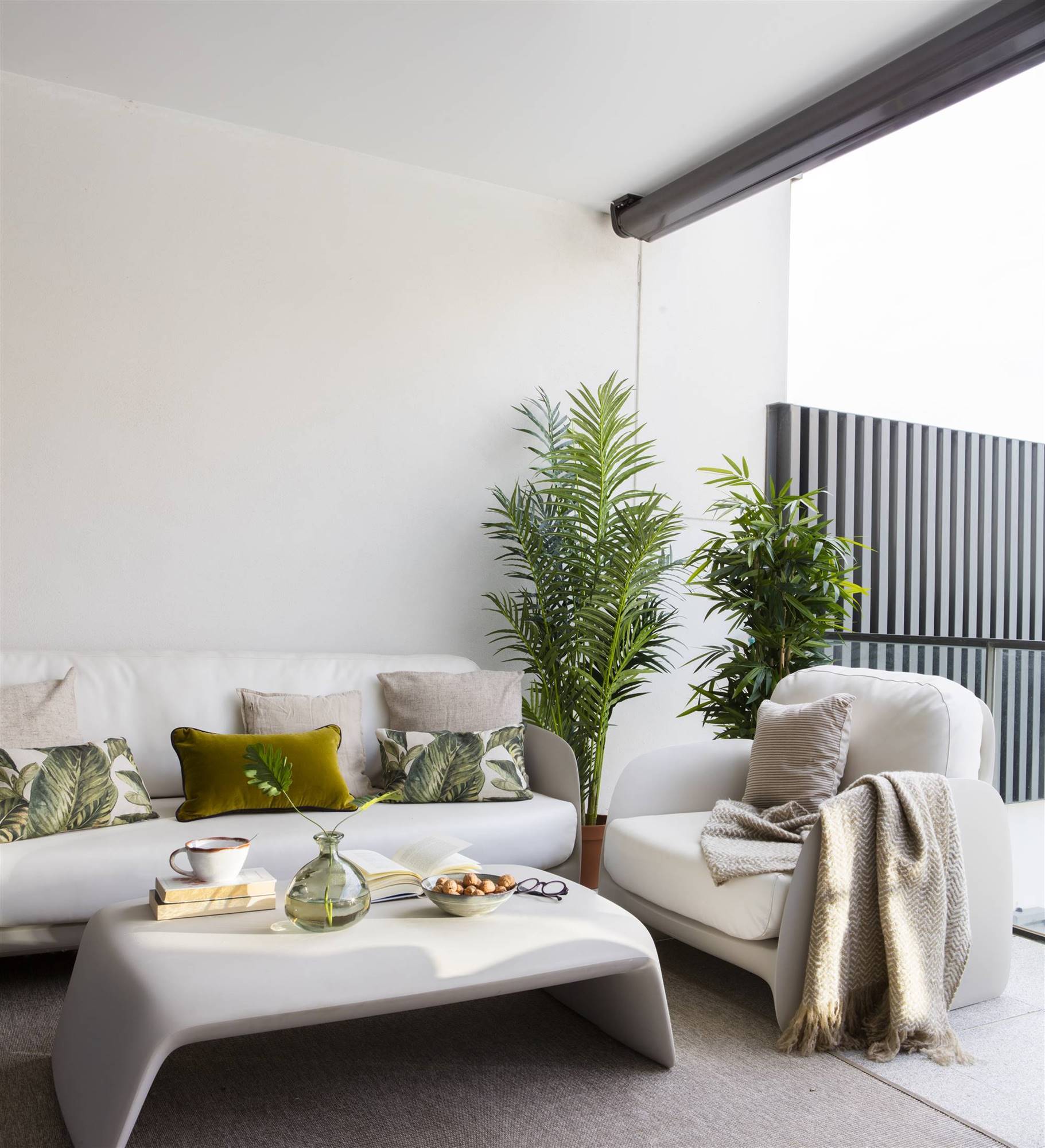 Terraza moderna con zona de estar con sofá, butaca y mesa de centro blancos. 