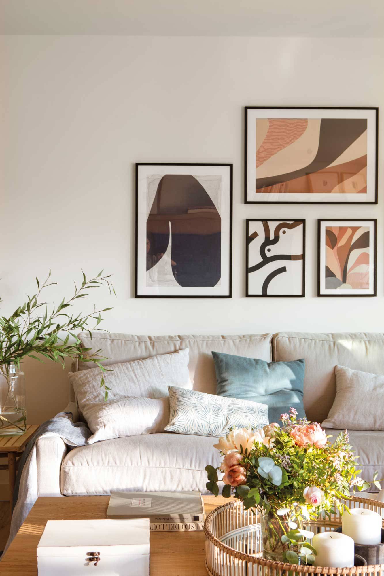 Salón con sofá de color beige con cuadros modernos en la pared. 