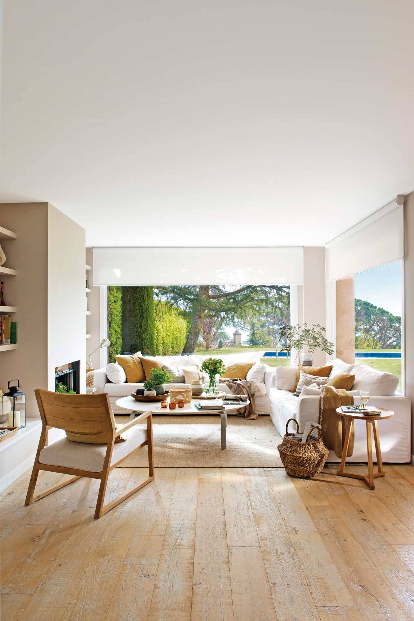 Salón con sofá grande, grandes ventanales y suelos de madera clara. 