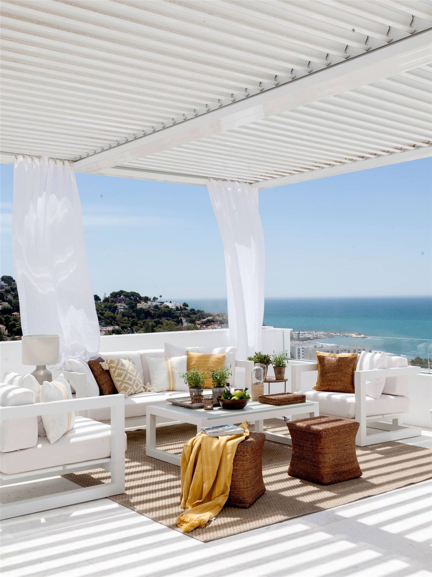 Terraza con pérgola y muebles blancos con vistas al mar. 