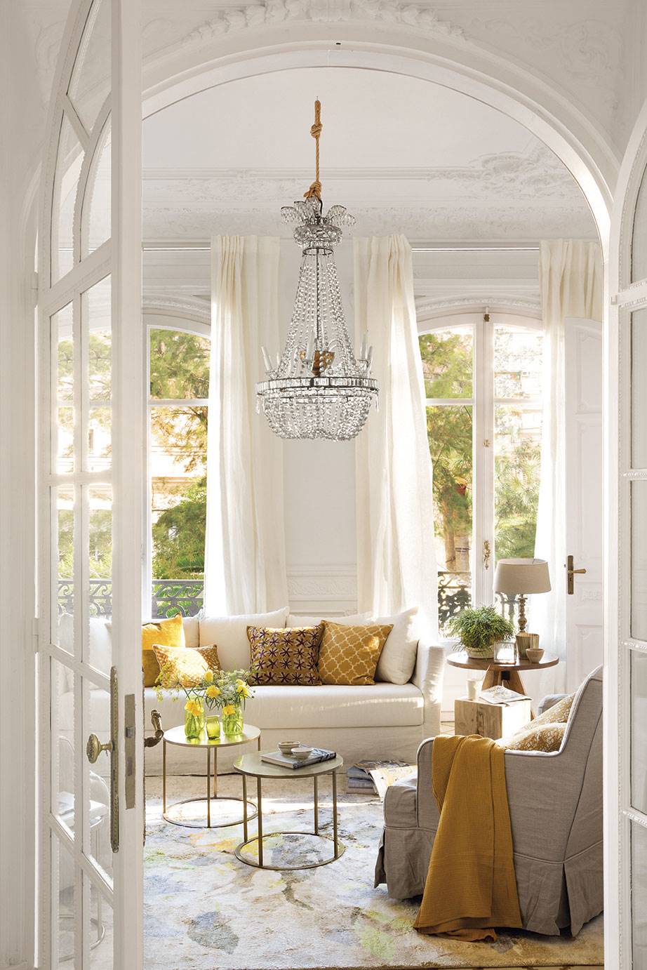 Salón de estilo clásico con sofá blanco, lámpara de araña y detelles en dorado. 
