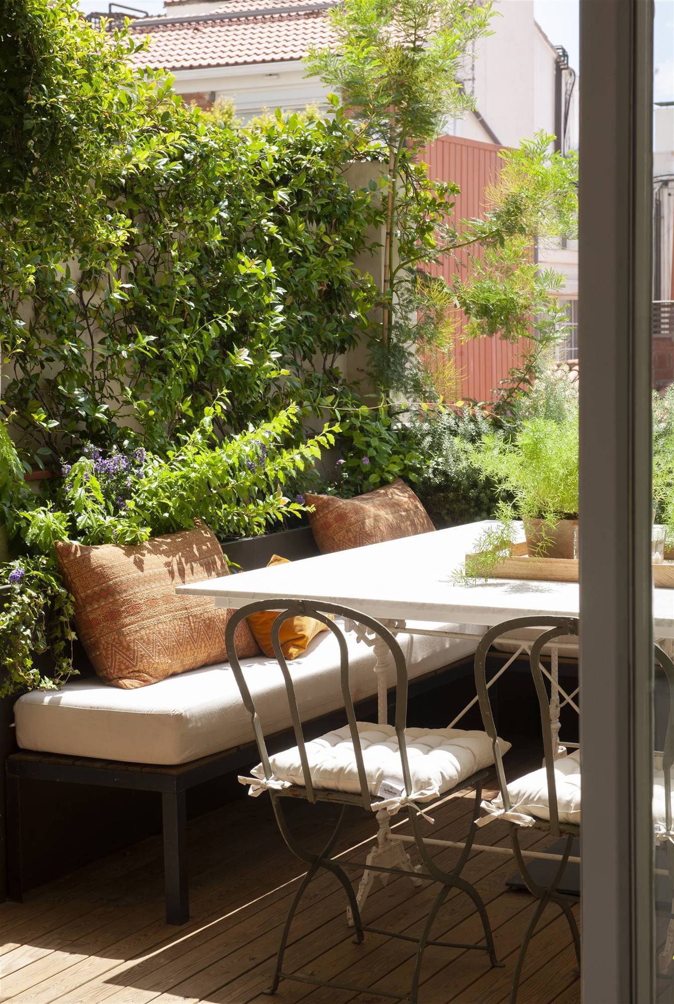Terraza con un jardín vertical y decorado con un banco, mesa y sillas de metal. 