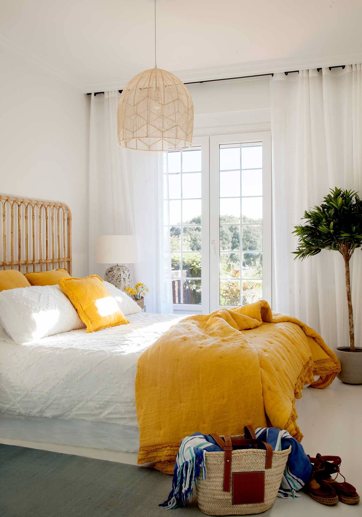 Dormitorio pequeño con cabecero de bambú y ropa de cama blanca y mostaza.