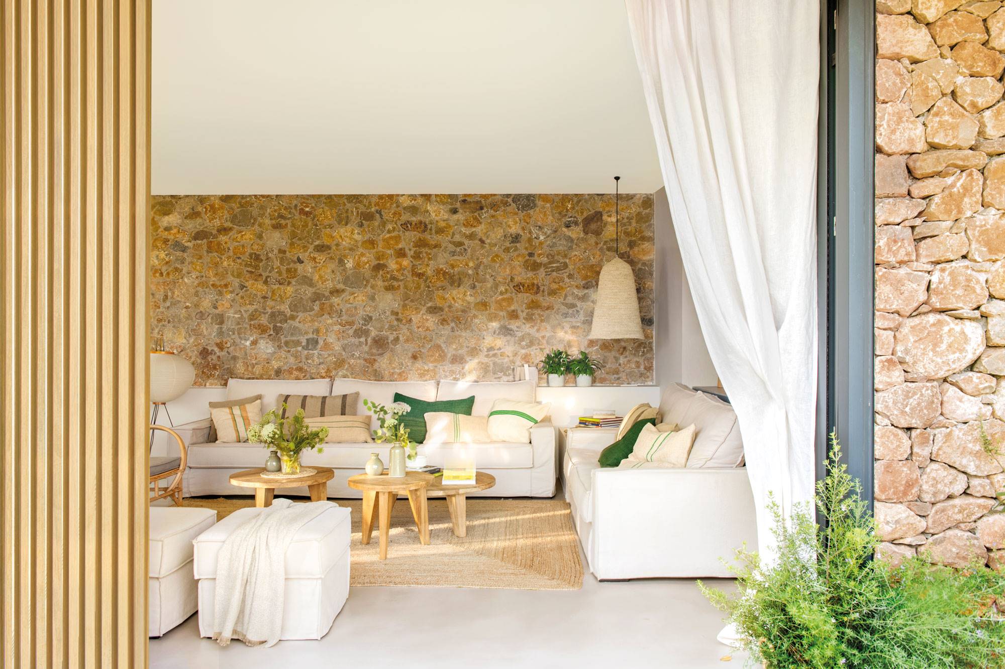 Salón de verano con paredes de piedra y sofás blancos. 
