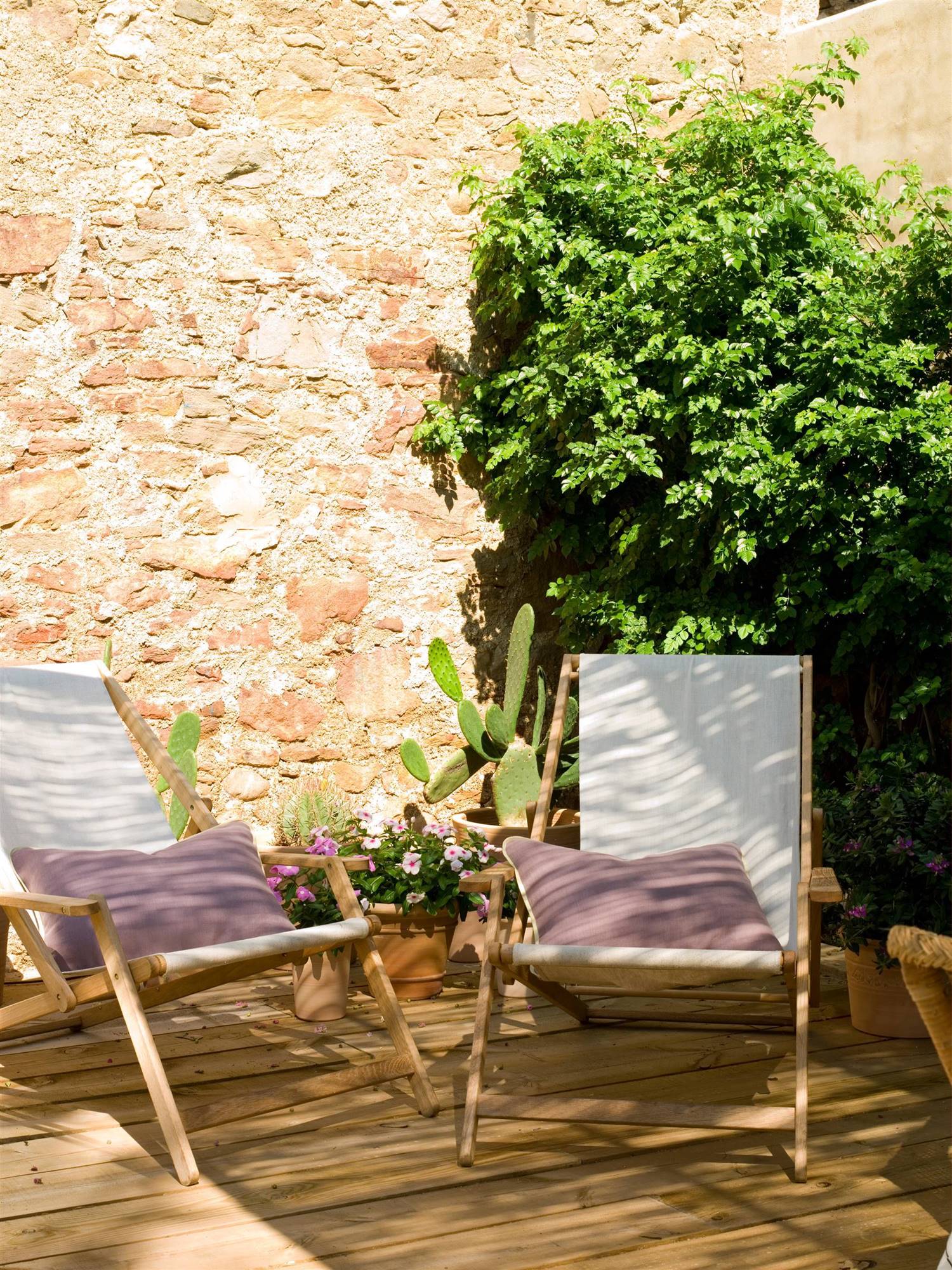 Tumbonas con respaldo de tela en un patio con paredes de piedra. 