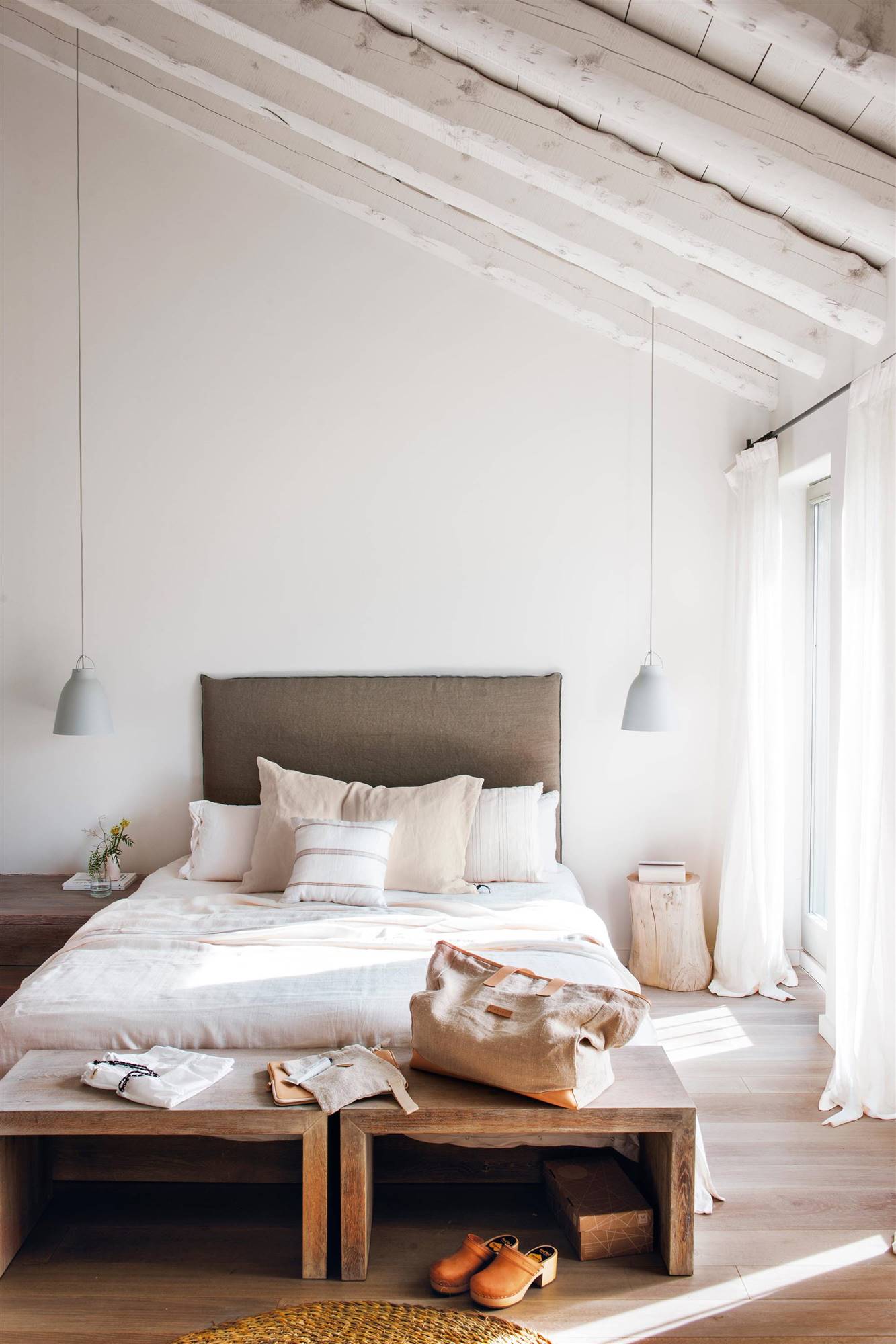 Dormitorio minimalista con cabecero de lino gris y banquetas de madera. 
