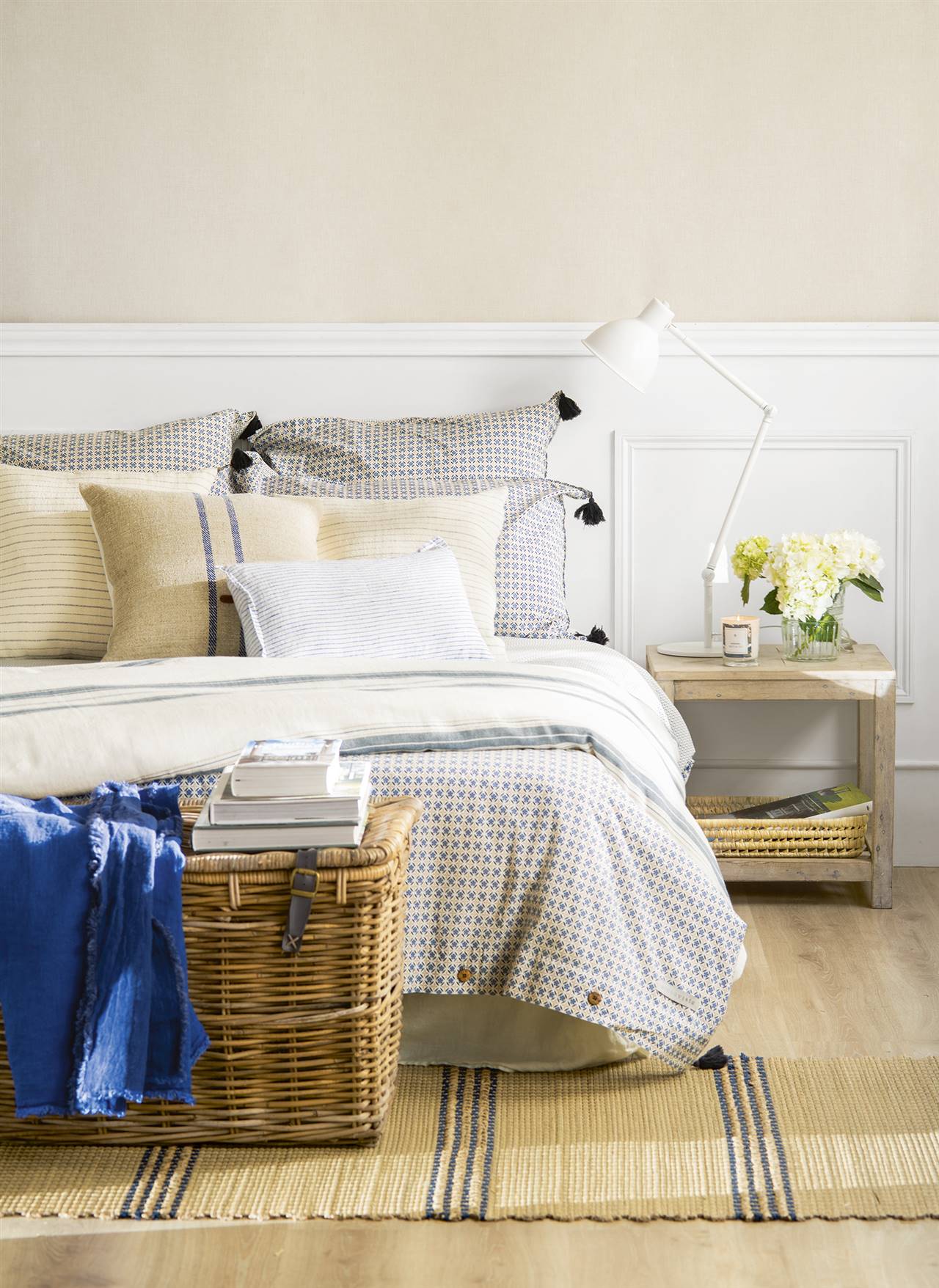 Dormitorio de estilo natural con baúl de mimbre, mesita de noche de madera y alfombra de fibras.