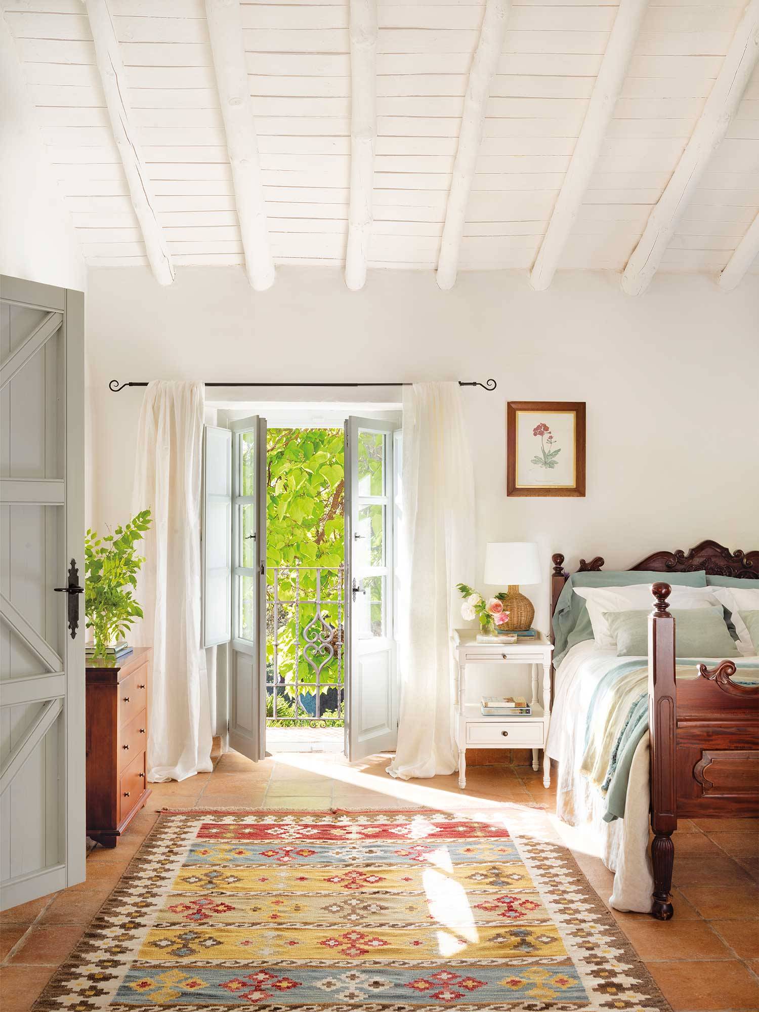 Dormitorio de verano de estilo clásico con alfombra kilim y estructura de cama de madera oscura. 
