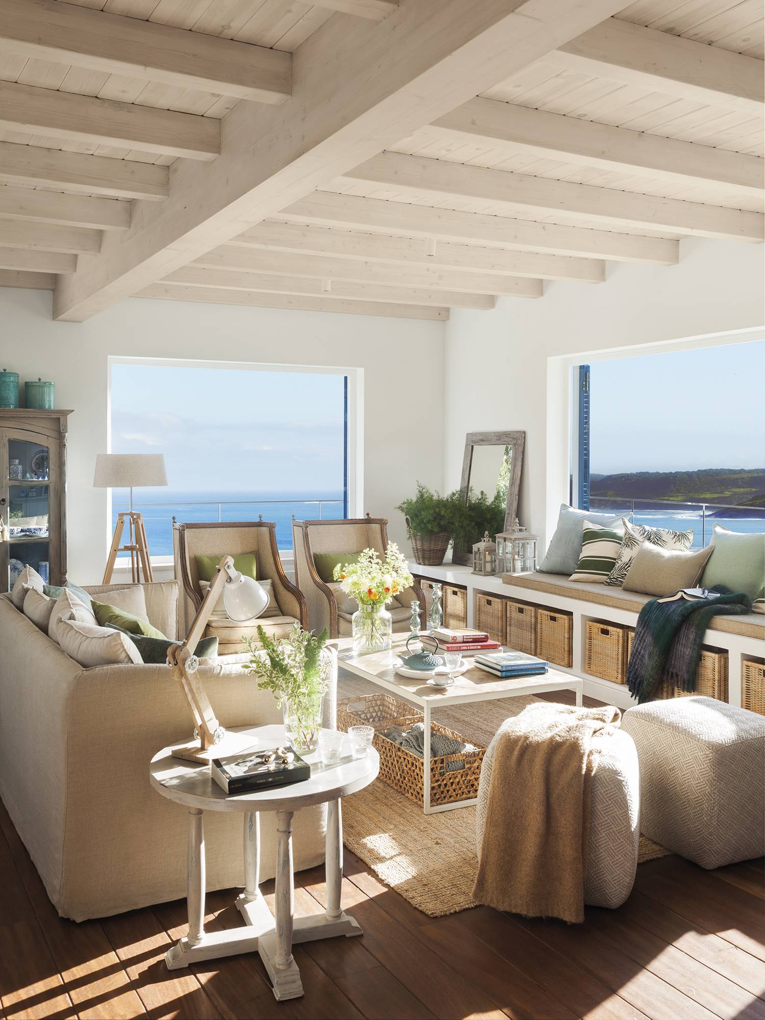 Salón con sofás beige y grandes ventanales con vistas al mar. 