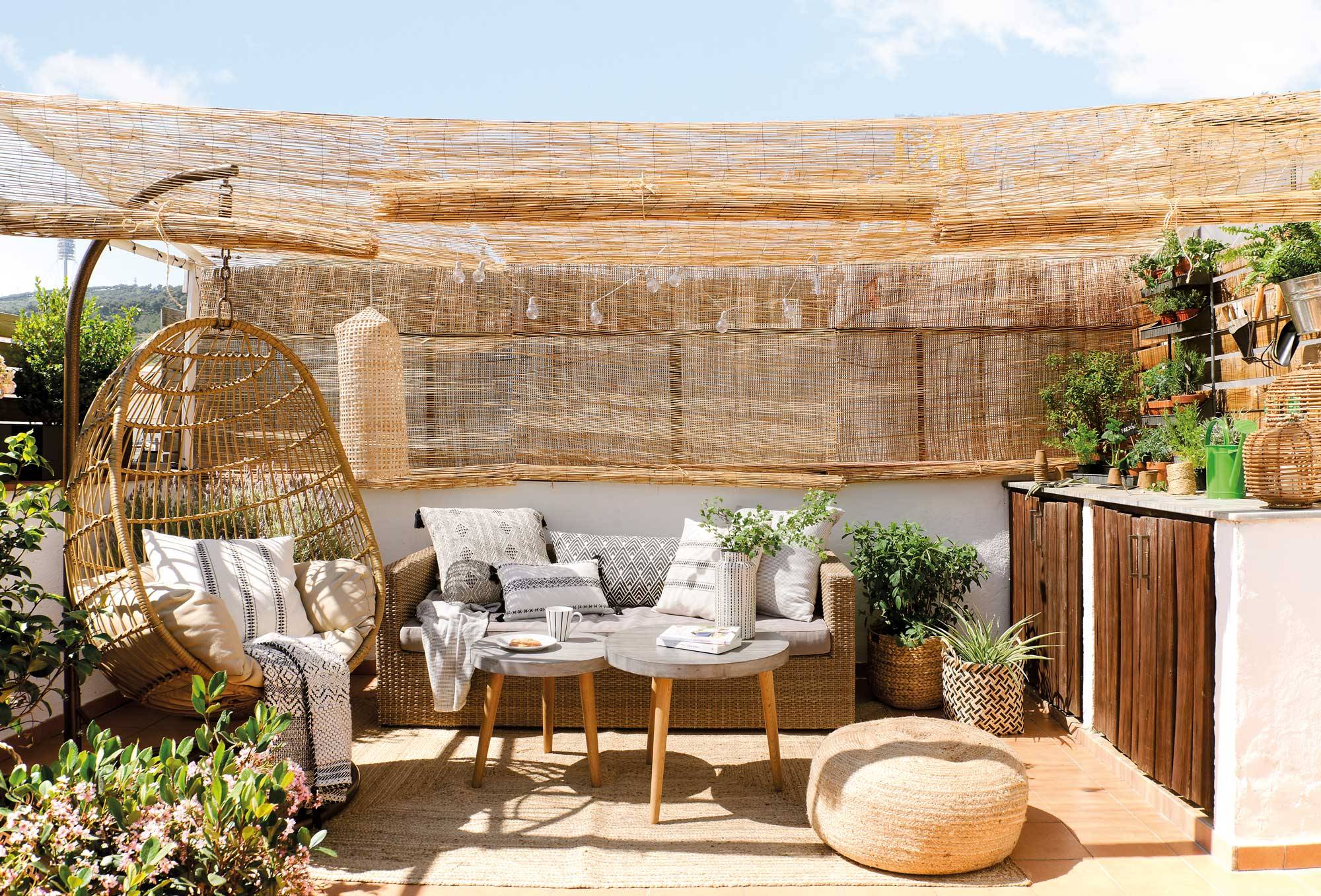 Rincón chill out en terraza con sofá de fibra, mesas de centro en madera y cemento y sillón balanc��n.