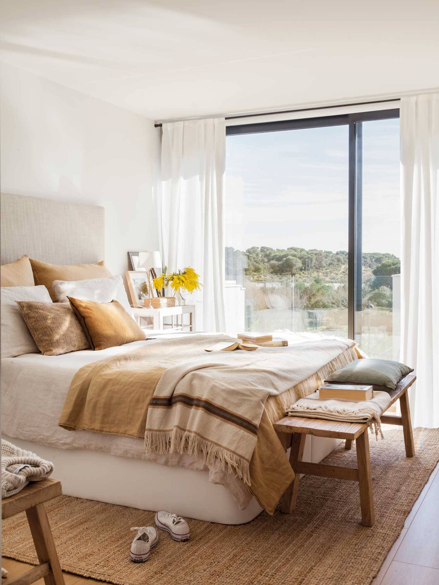 Dormitorio decorado en tonos tierra con banco de madera y alfombra de fibras. 
