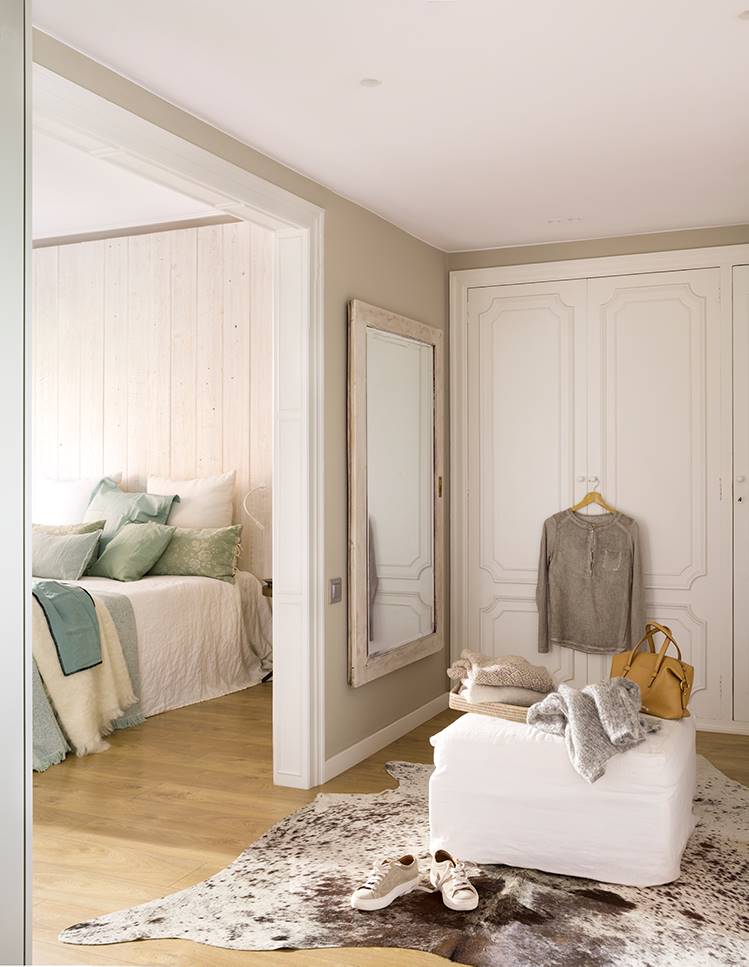 Vestidor junto al dormitorio con armarios blancos, espejo, puf y alfombra